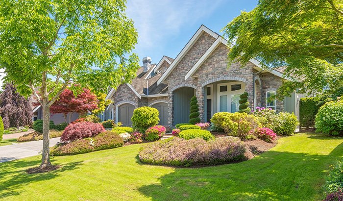 Suburban house with a well-kept lawn and colorful landscaping, including trees, bushes, and flowering plants cared for by Speer mowing.
