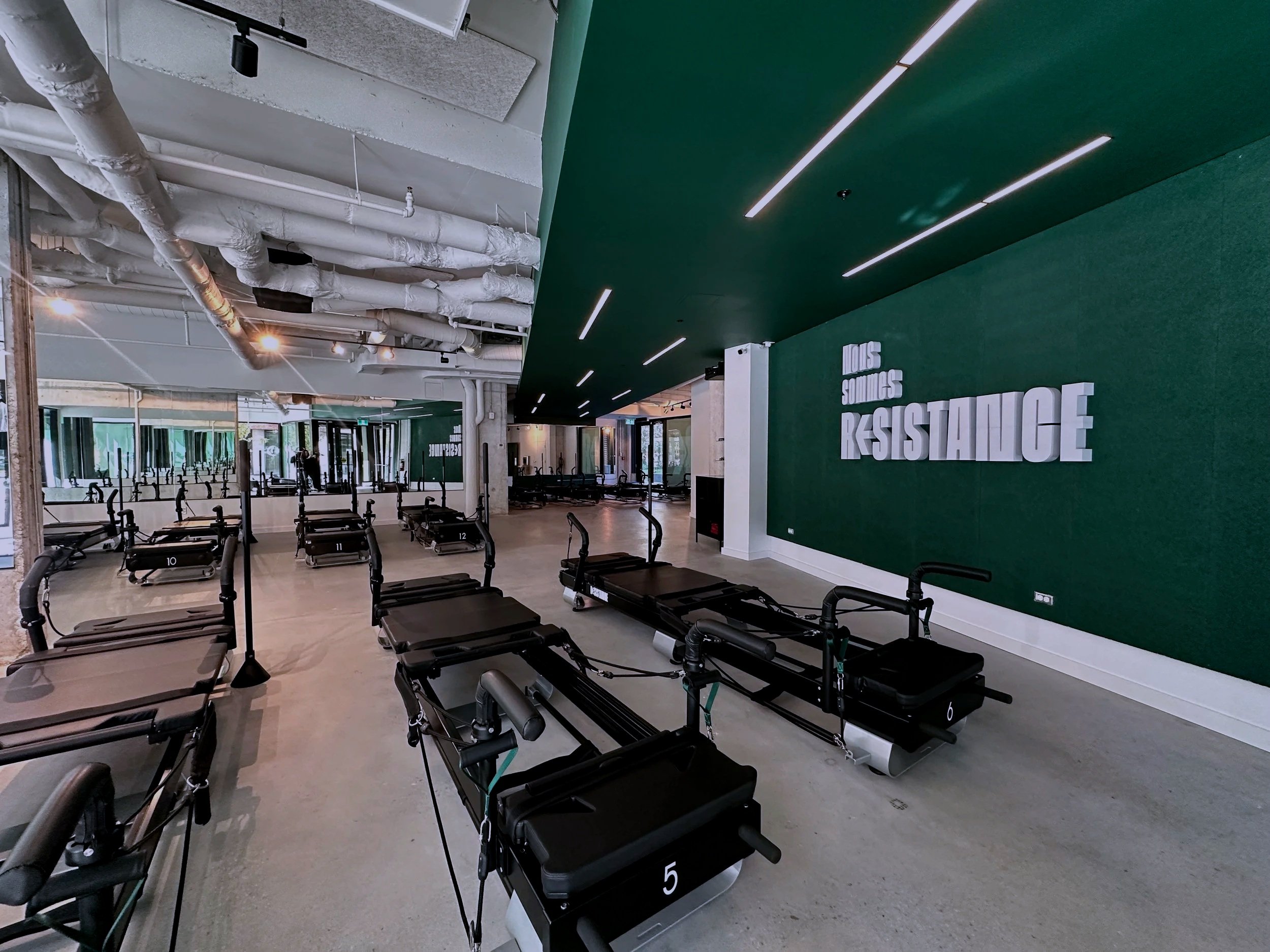 Empty Pilates studio with Xformer machines and a green wall displaying the words 'Nous sommes resistance' in white 3D letters.