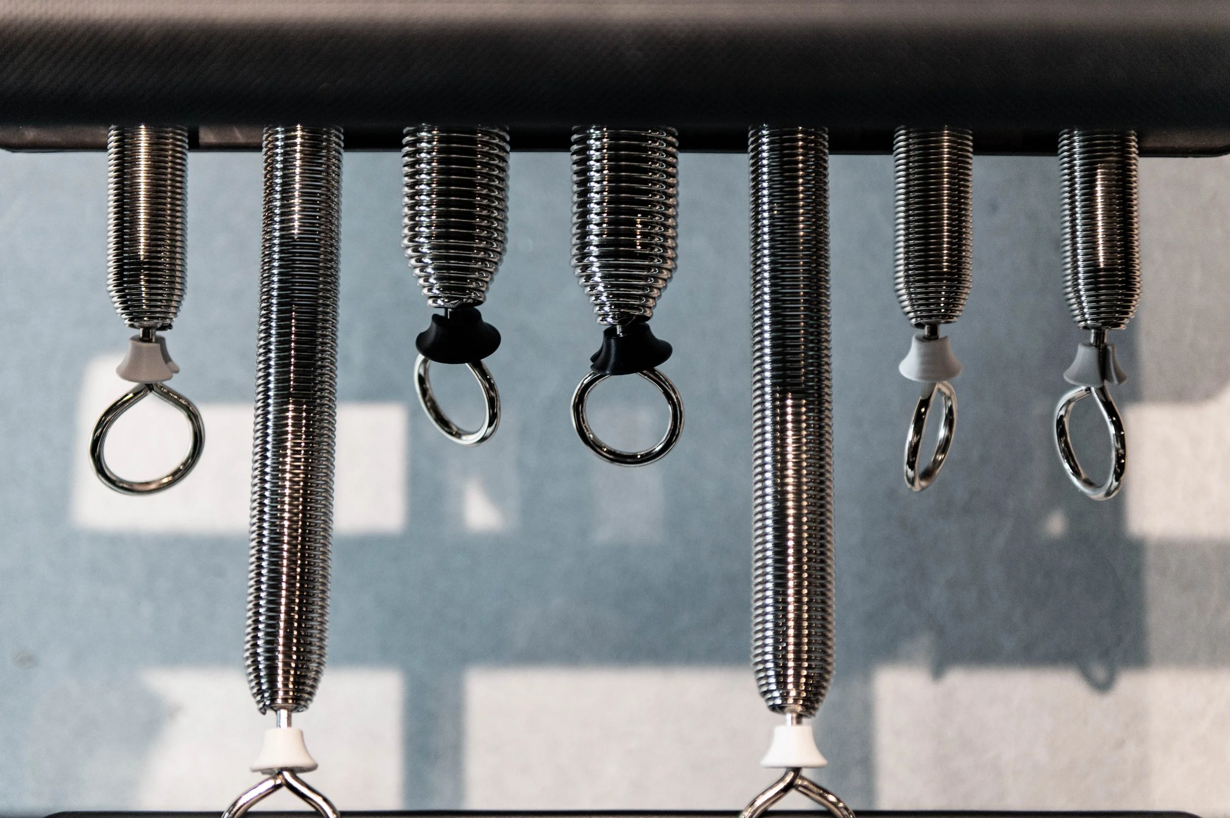 A row of metal springs with attached rings hanging underneath from a black horizontal bar.