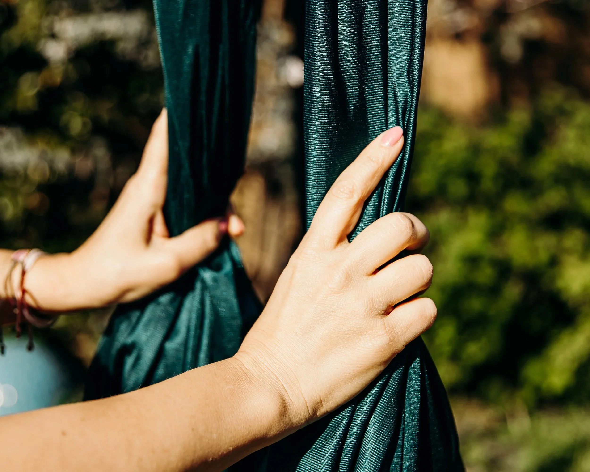 Deux bras, dont un avec une peau claire et l'autre avec une peau plus foncée, se croisent. La personne avec la peau claire porte un bracelet rouge, et la personne avec la peau plus foncée porte un bracelet noir. Les bras sont en contact sur un fond flou montrant des arbres ou des buissons.