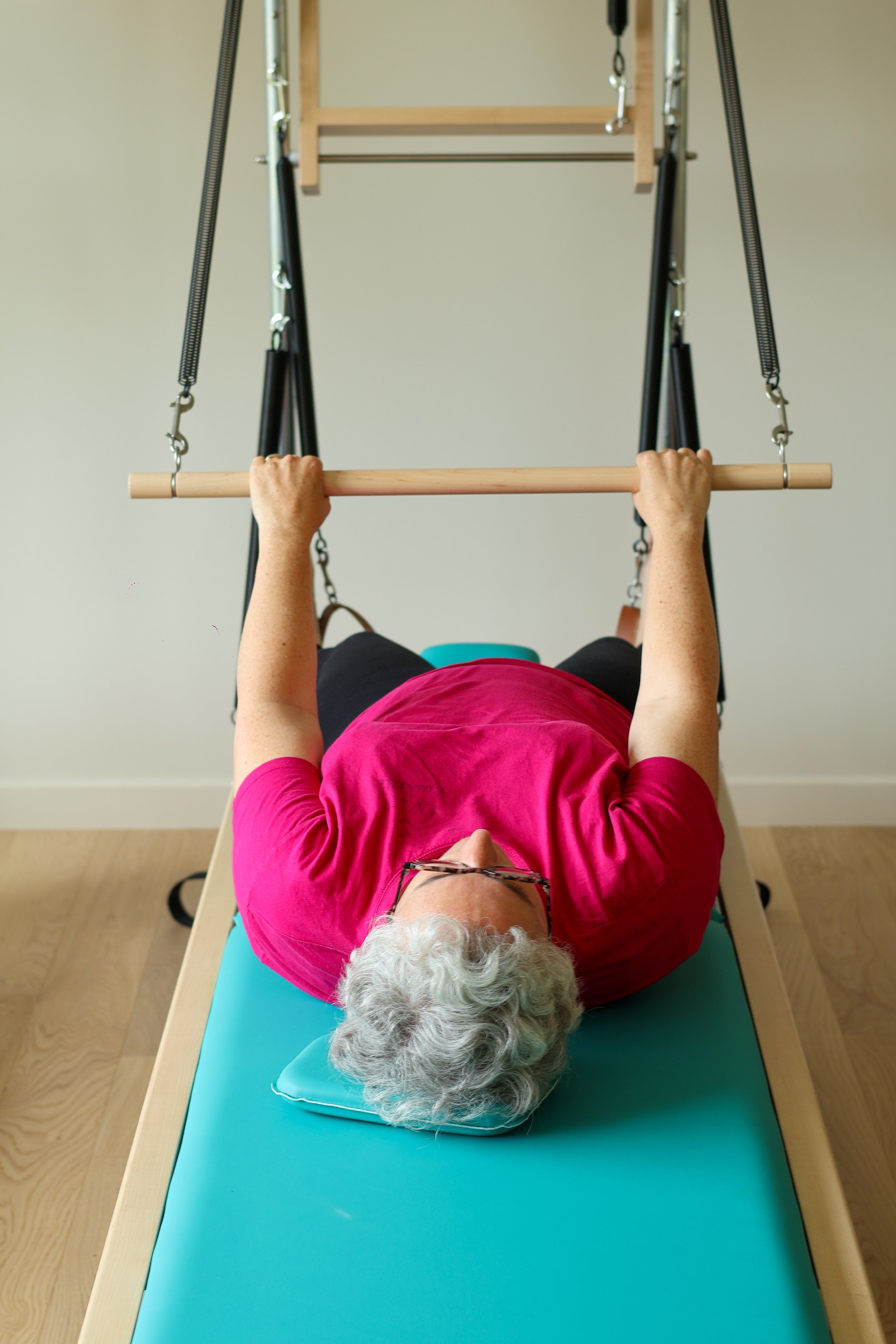 Une personne allongée sur un tapis de REFORMER avec une barre en bois et ressort pendant cours pilates 