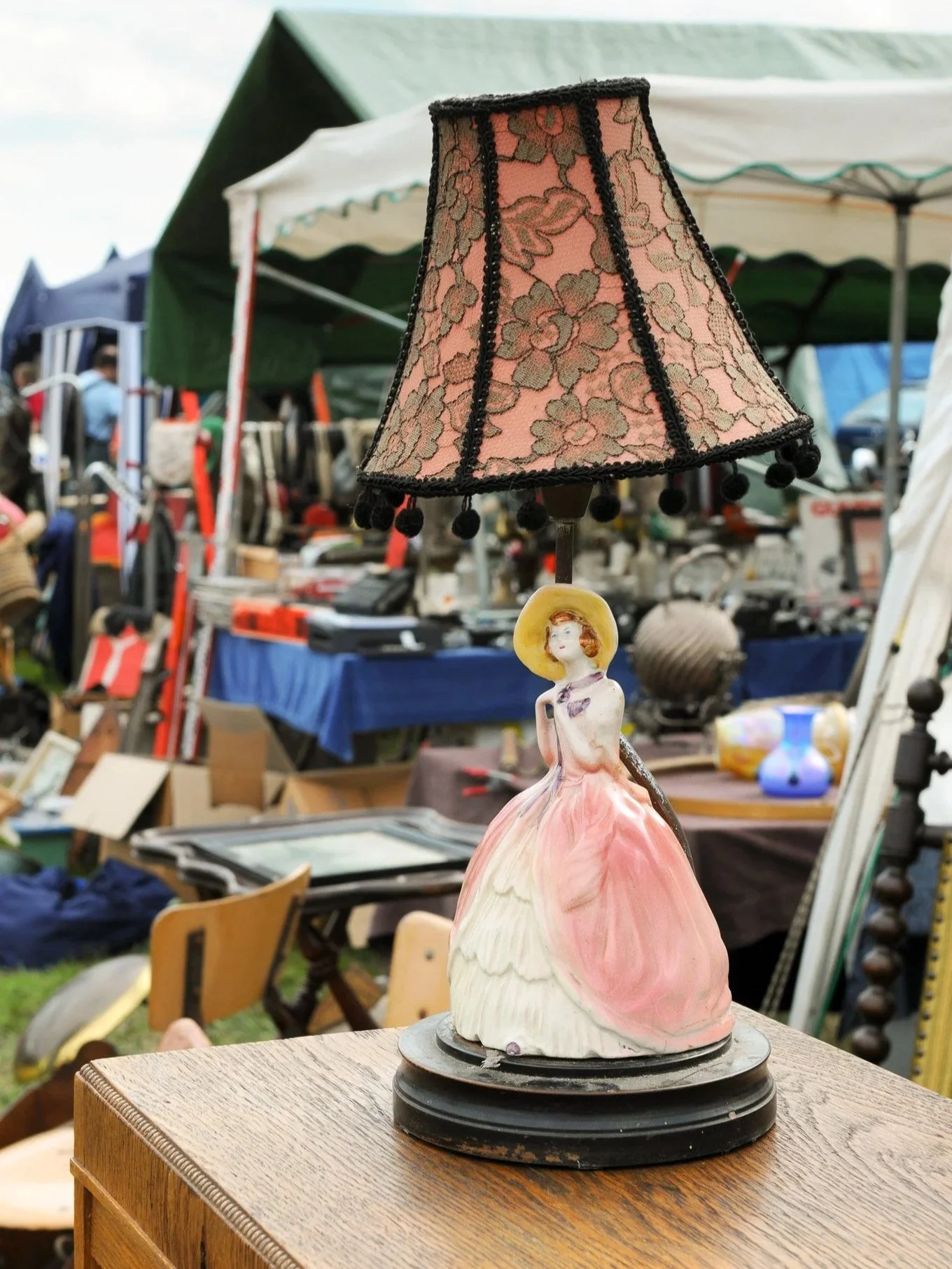 Ceramic lamp shaped like a woman in a pink dress with a wide-brimmed hat, topped with a pink lace lampshade with black trim.