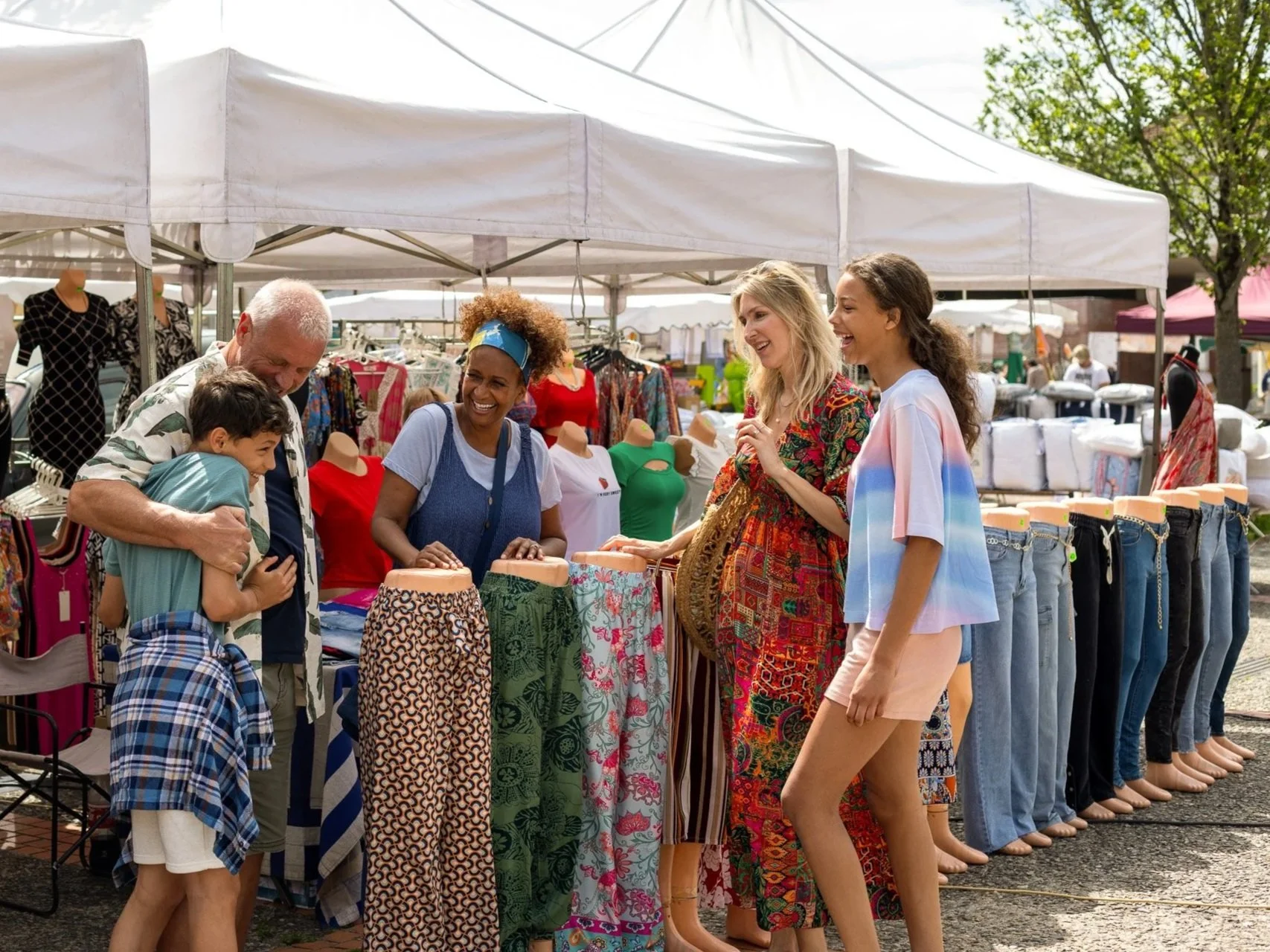 People shopping at an outdoor market stall with clothing items on display, engaging and smiling.