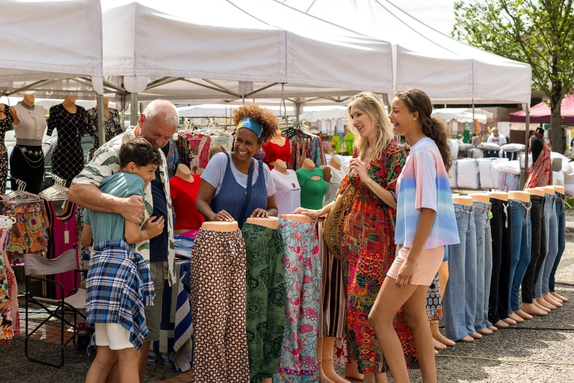 People shopping at an outdoor market, looking at clothing and mannequin displays.