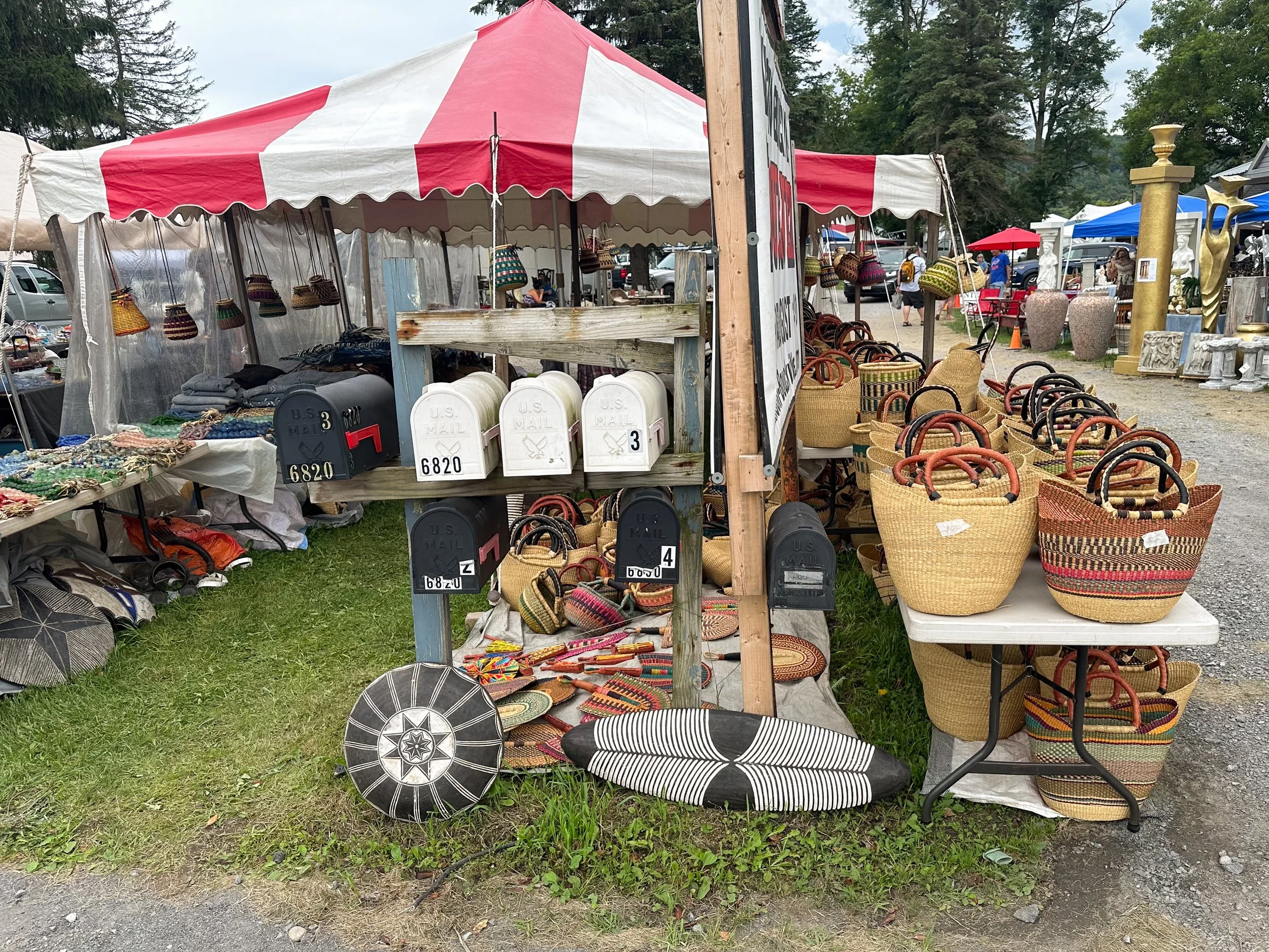 Outdoor market stall with colorful woven baskets and mailboxes, selling handmade crafts and accessories.