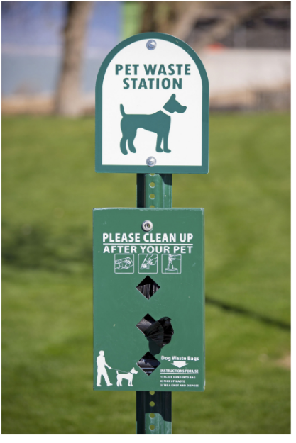 Pet waste station with a sign of a dog silhouette and instructions to clean up after your pet, including dog waste bags inside a dispenser. commercial and residential dog waste service