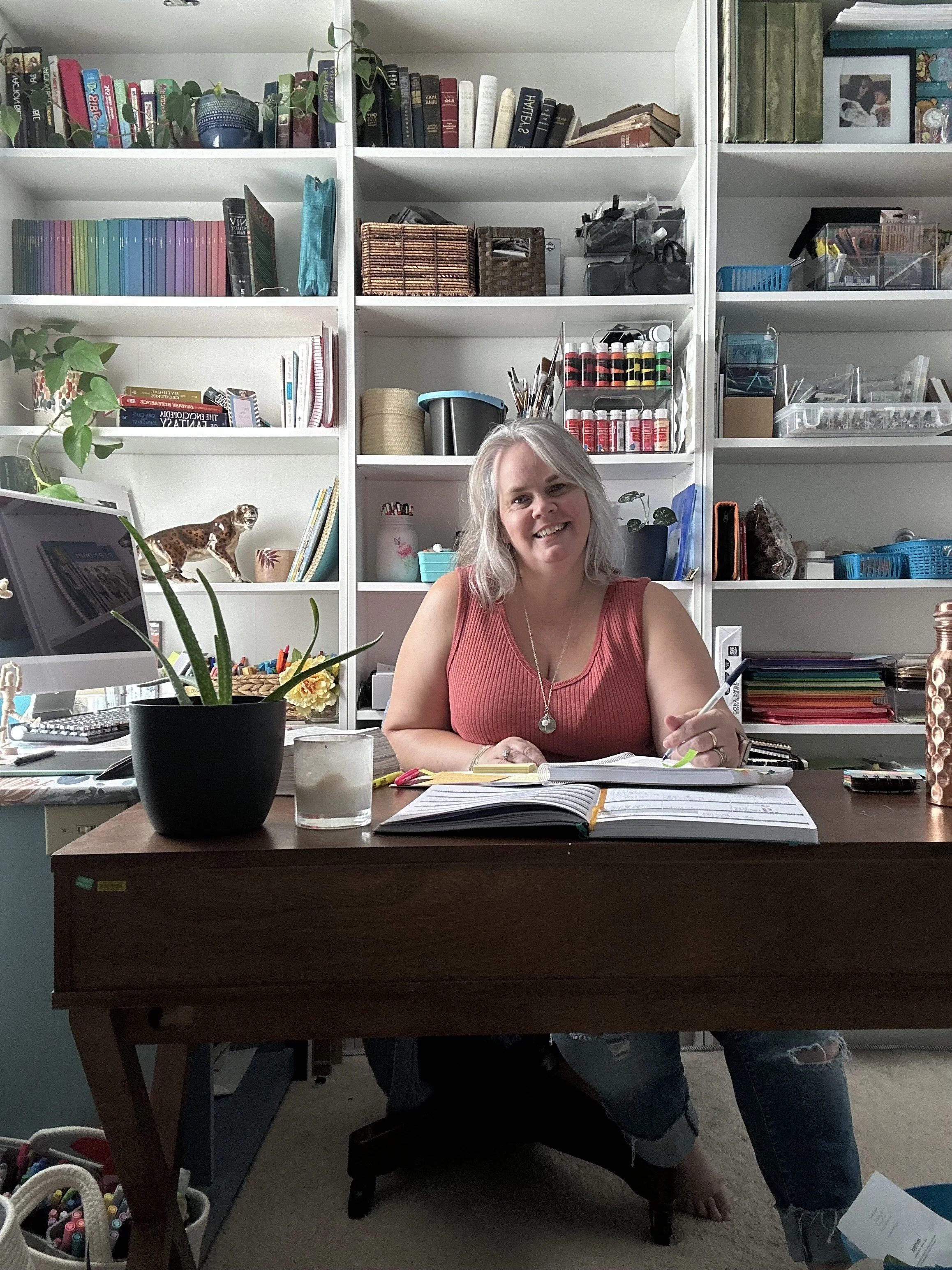grey haired woman seated at desk in front of bookshelves