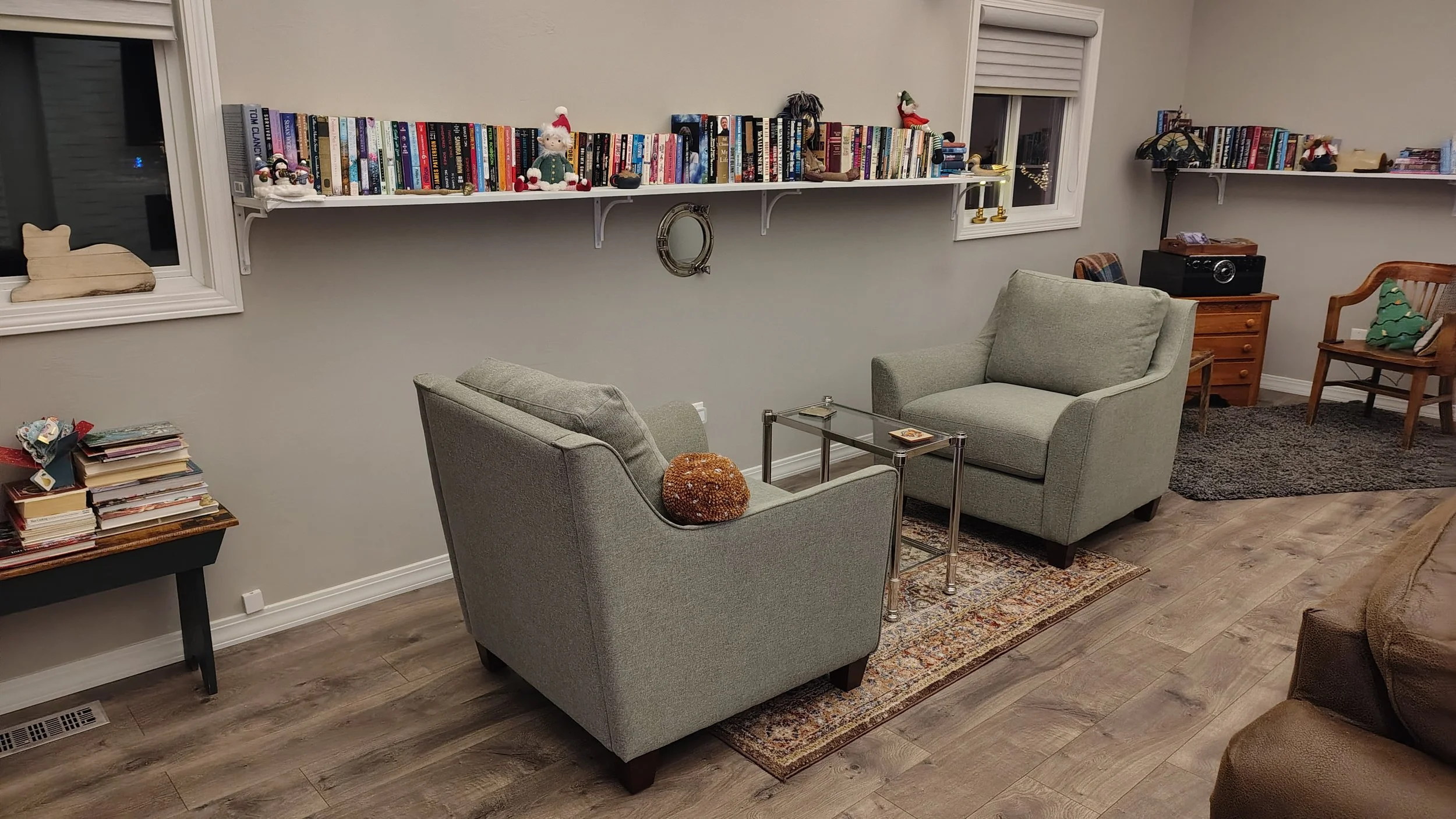 Living room with two light green armchairs, a glass coffee table, books on wall shelves, and Christmas decorations.