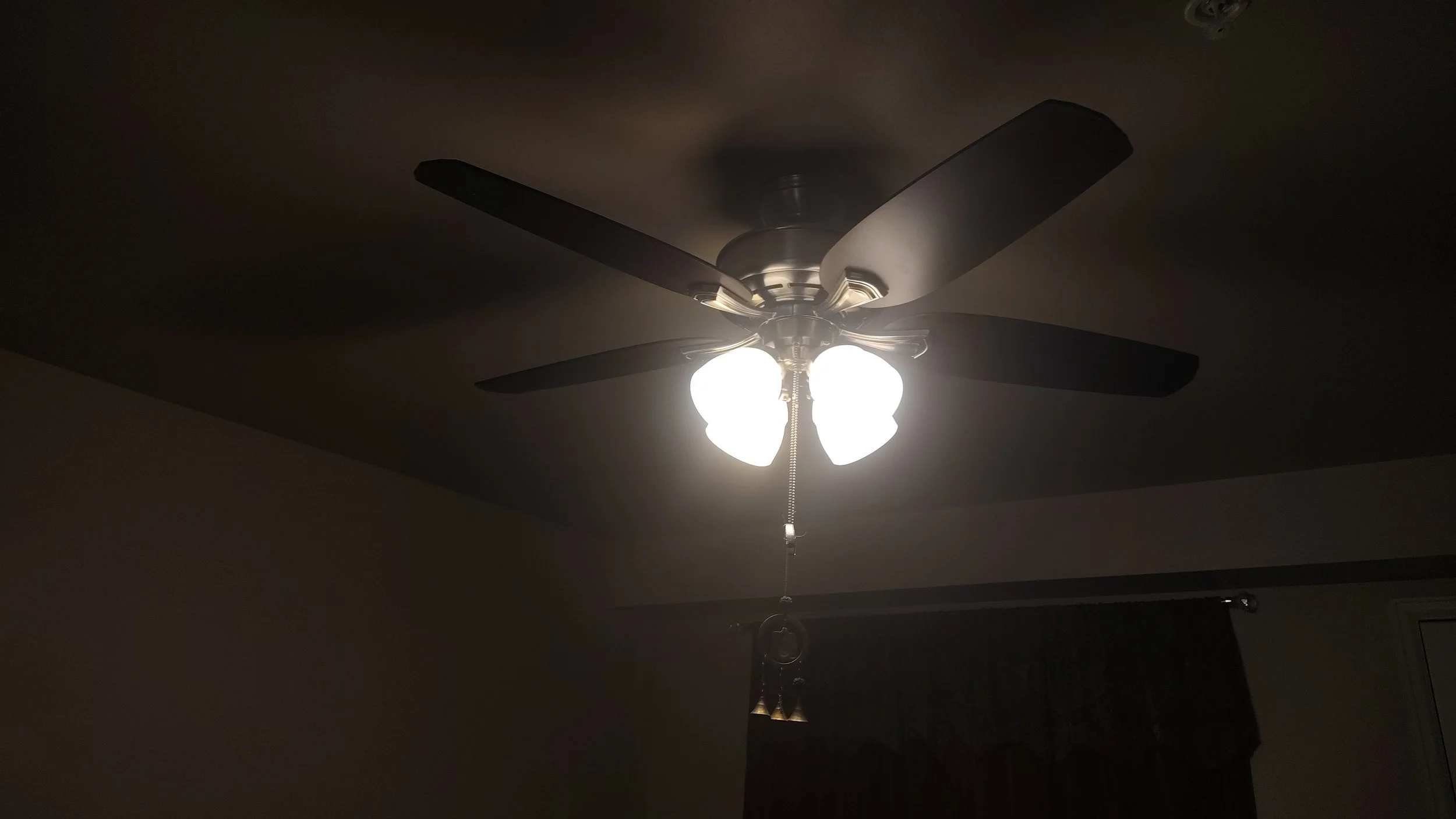 Ceiling fan with lights turned on in a dark room.