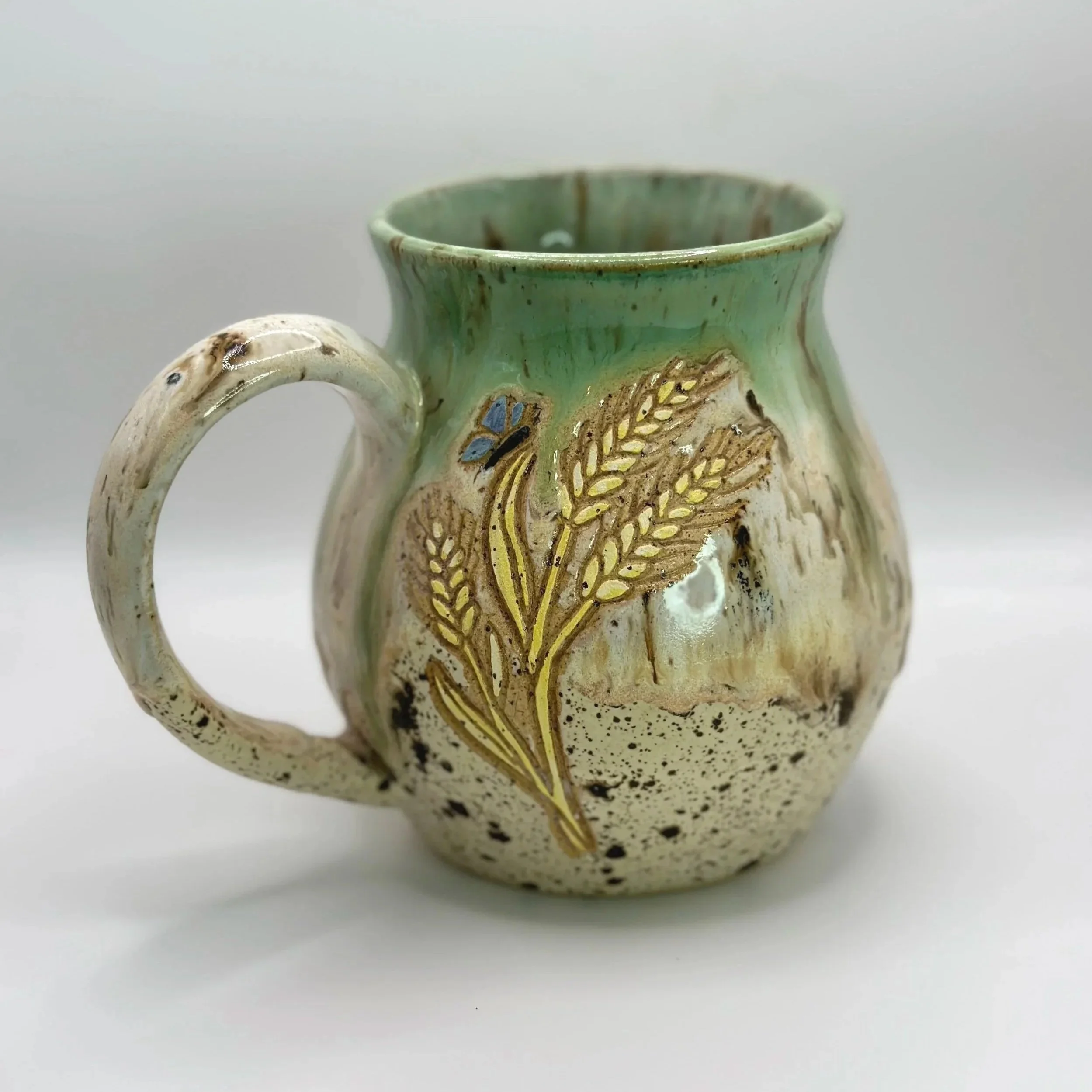 Ceramic mug with a floral design, green top, beige bottom, and wheat motifs.