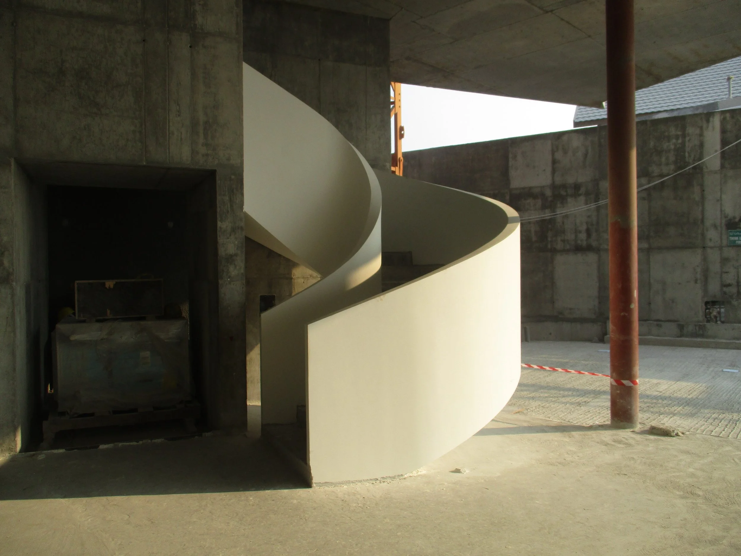 Modern white spiral staircase under construction in a concrete building.