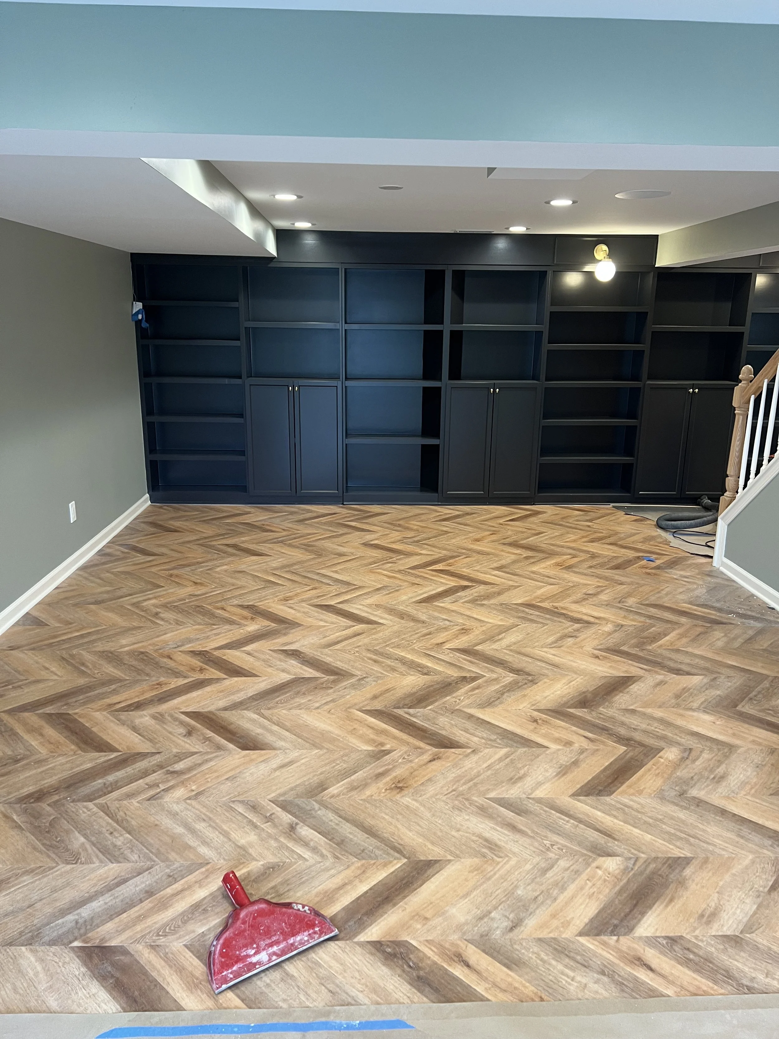 Empty room with hardwood floors, dark built-in shelves, and a staircase to the right. A dustpan is on the floor.