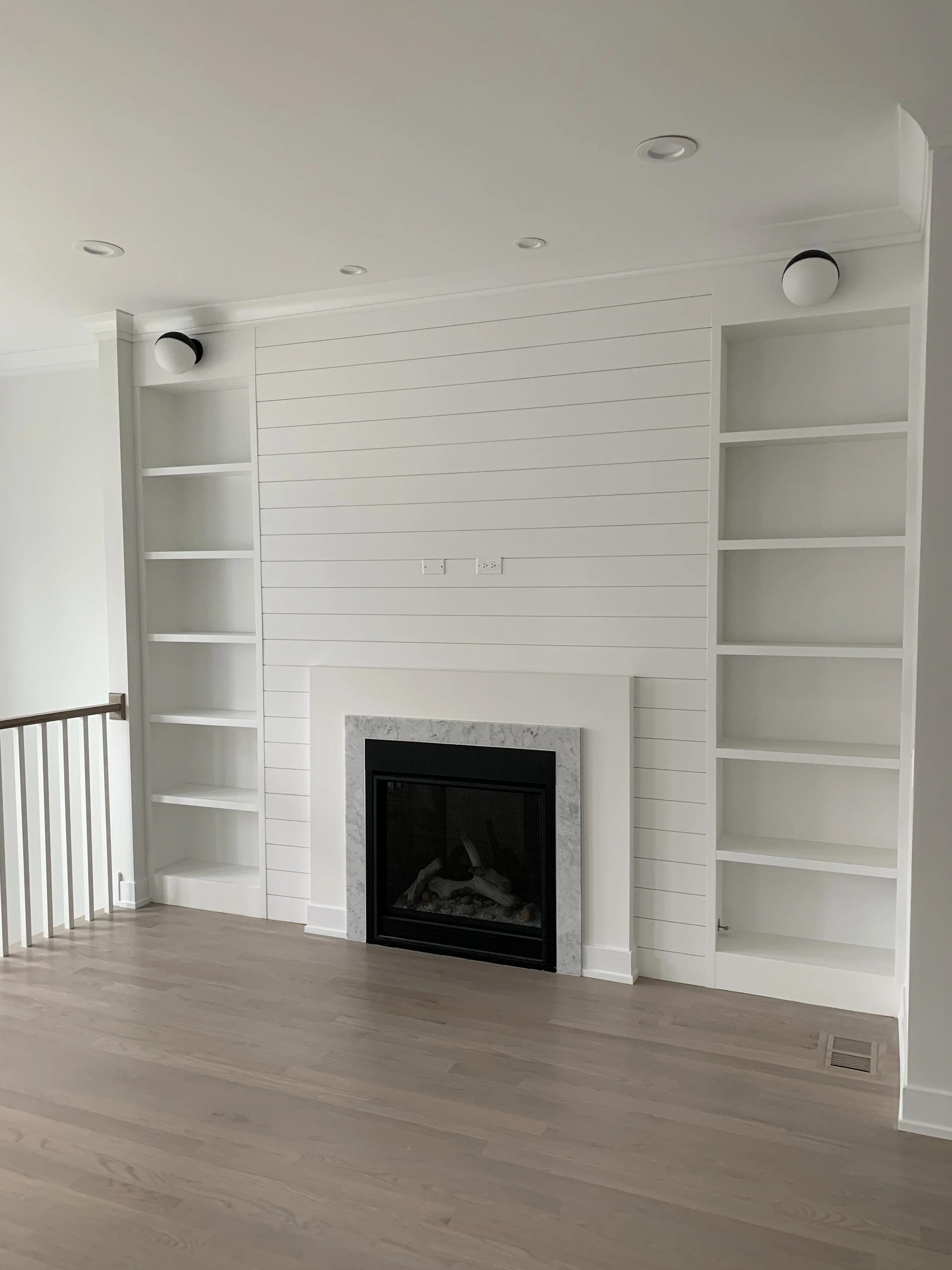 Living room with white built-in shelves, a fireplace with a marble surround, and light hardwood flooring.