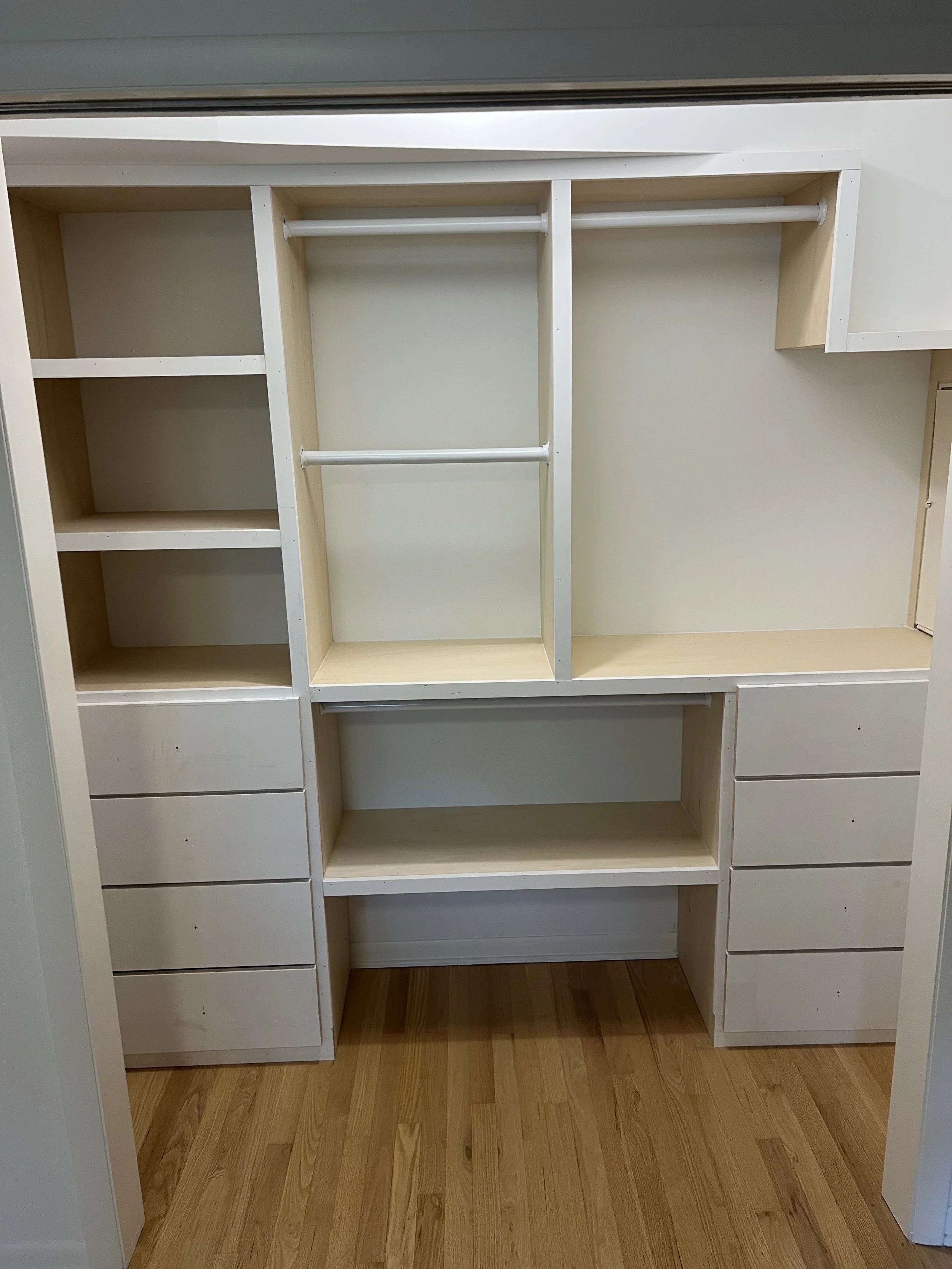 Empty custom closet with open shelves, drawers, and hanging rods, wooden flooring.