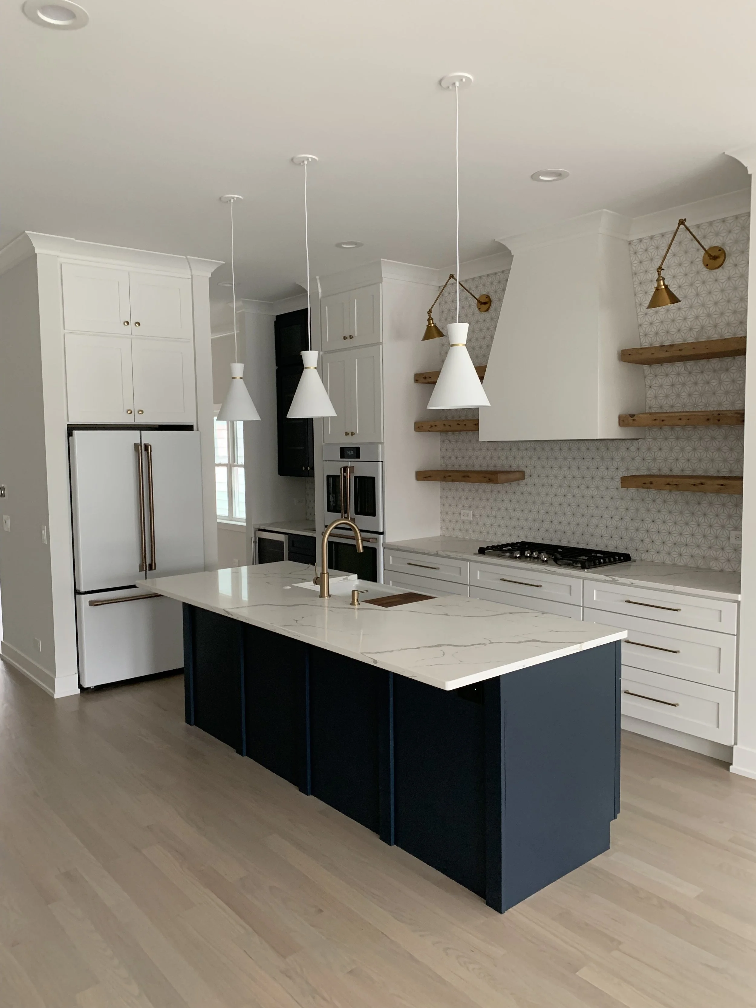 Modern kitchen with white cabinets, a marble island with navy blue base, gold fixtures, and open wooden shelves.