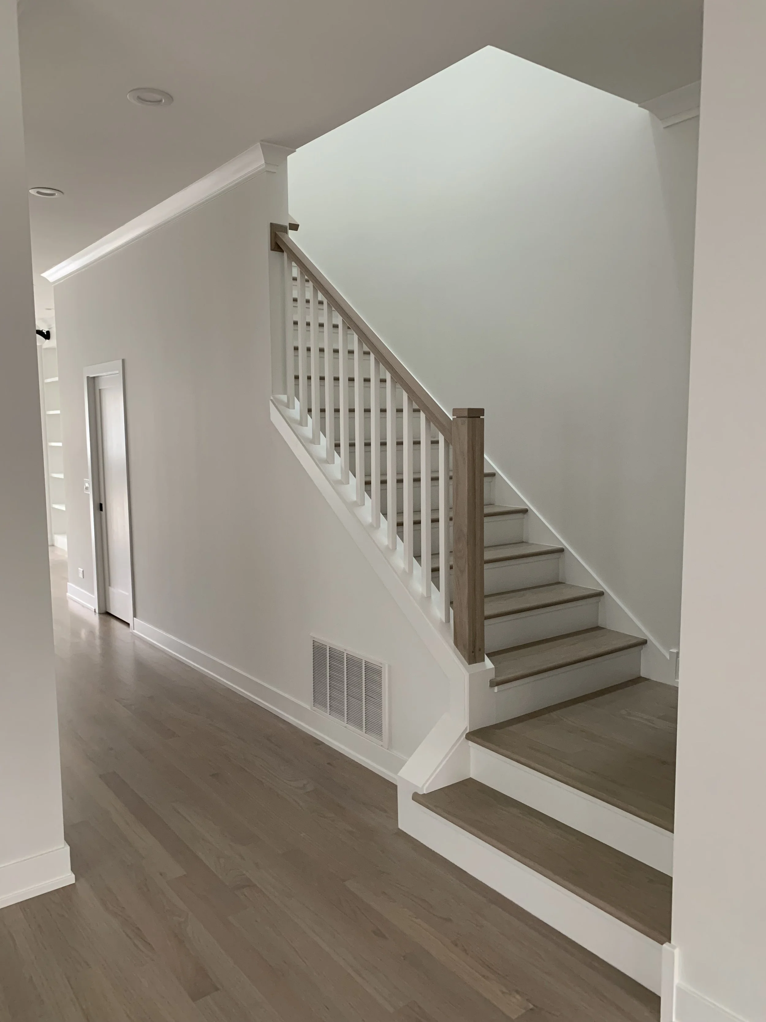 Interior view of a staircase with wooden steps and white railing inside a modern home with light-colored walls and hardwood flooring.