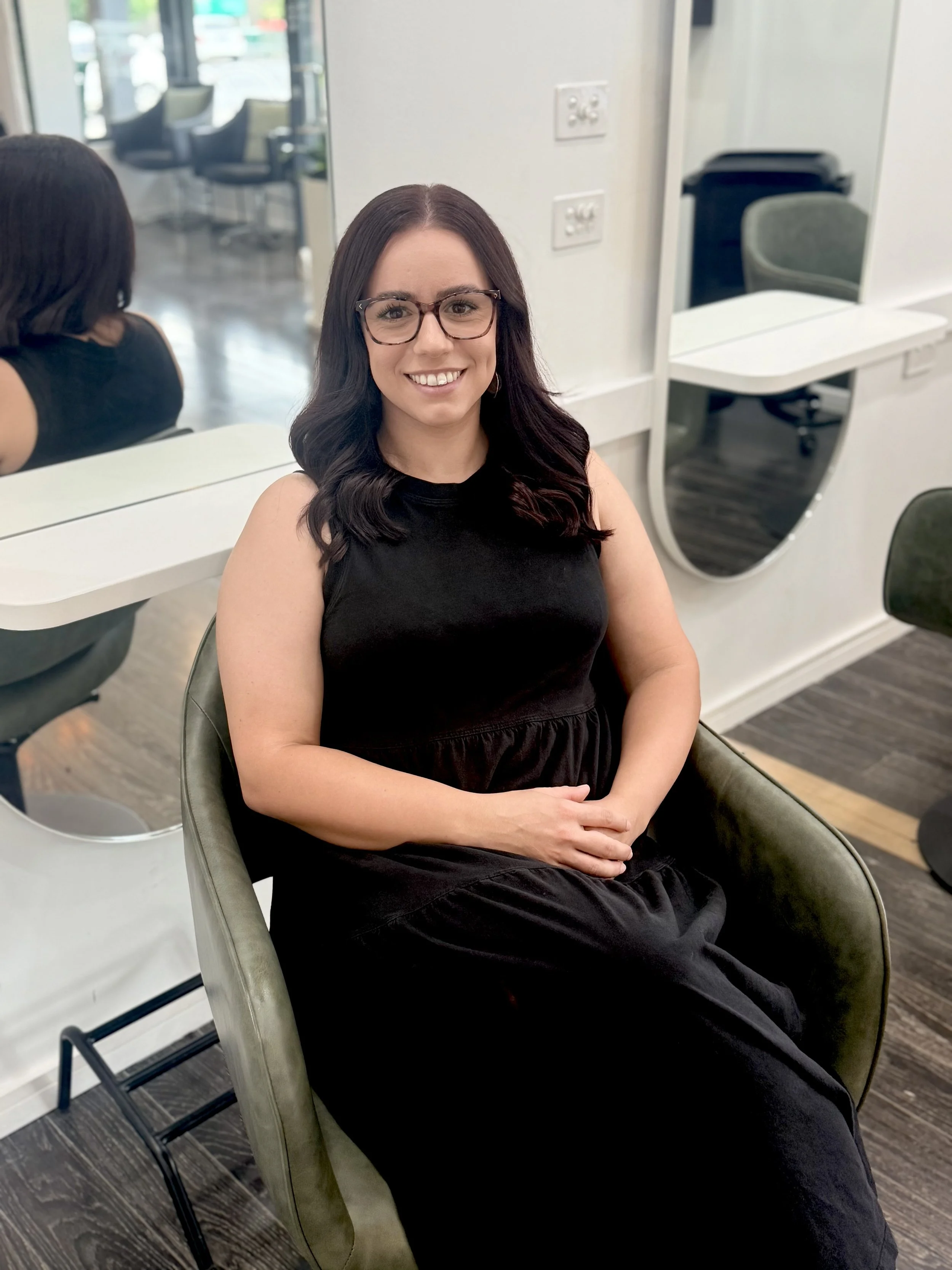 Taela sits in a salon chair, smiling at the camera