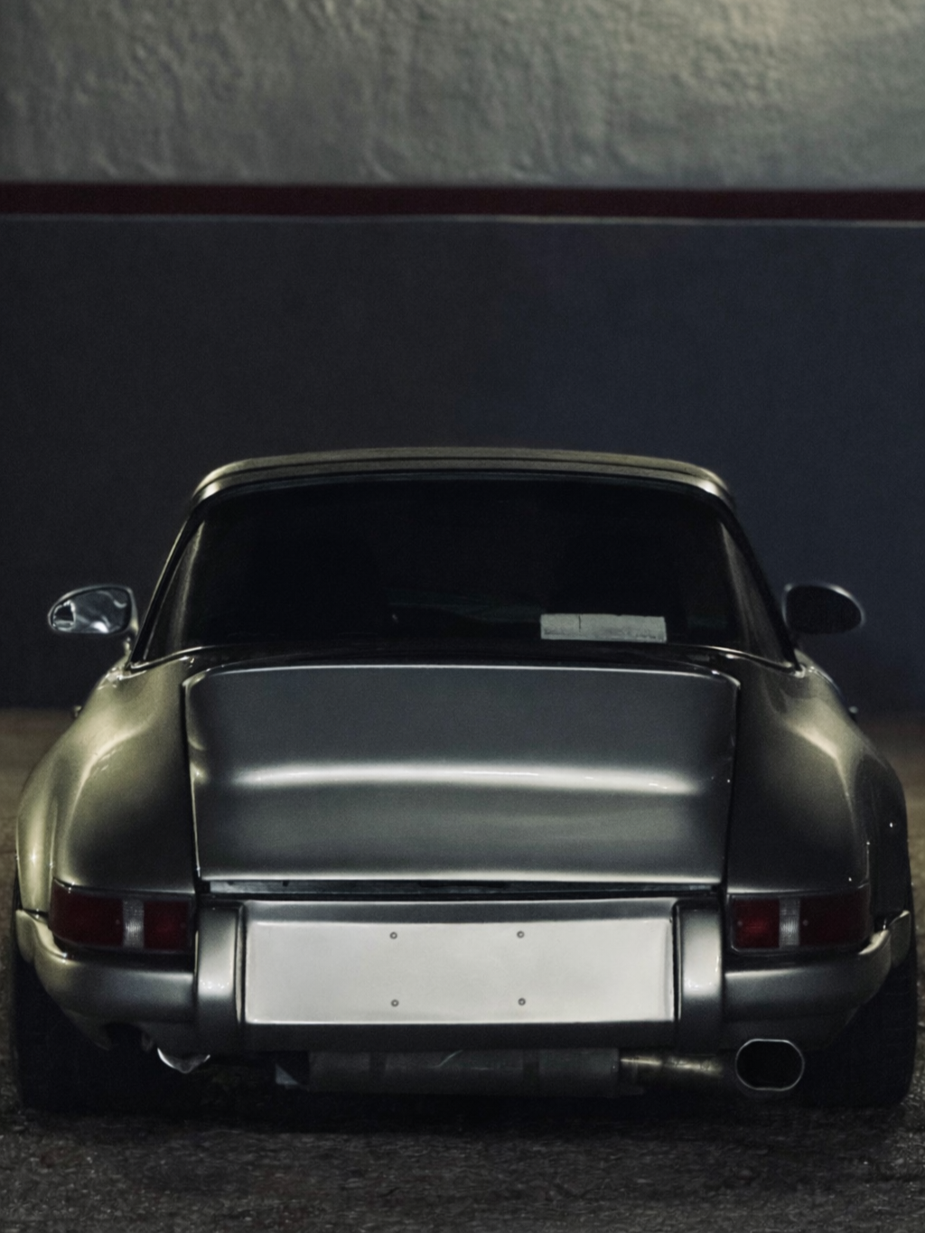 Rear view of a vintage silver sports car parked outdoors at night, with a dark background and minimal lighting highlighting its sleek curves.