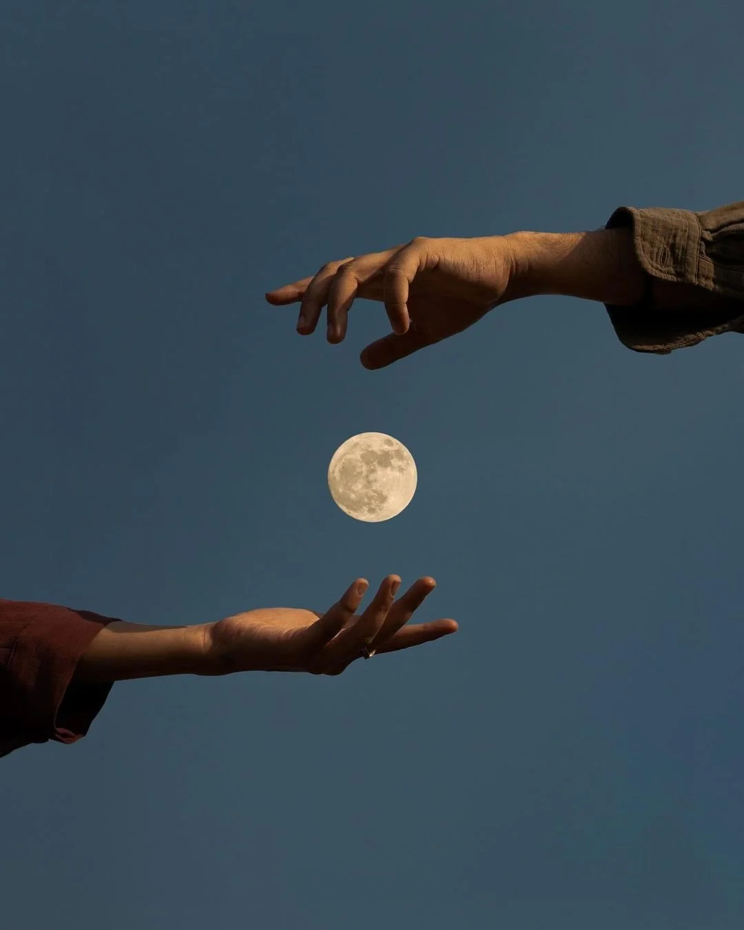 Two hands reaching towards each other with the moon between them against a dark sky.