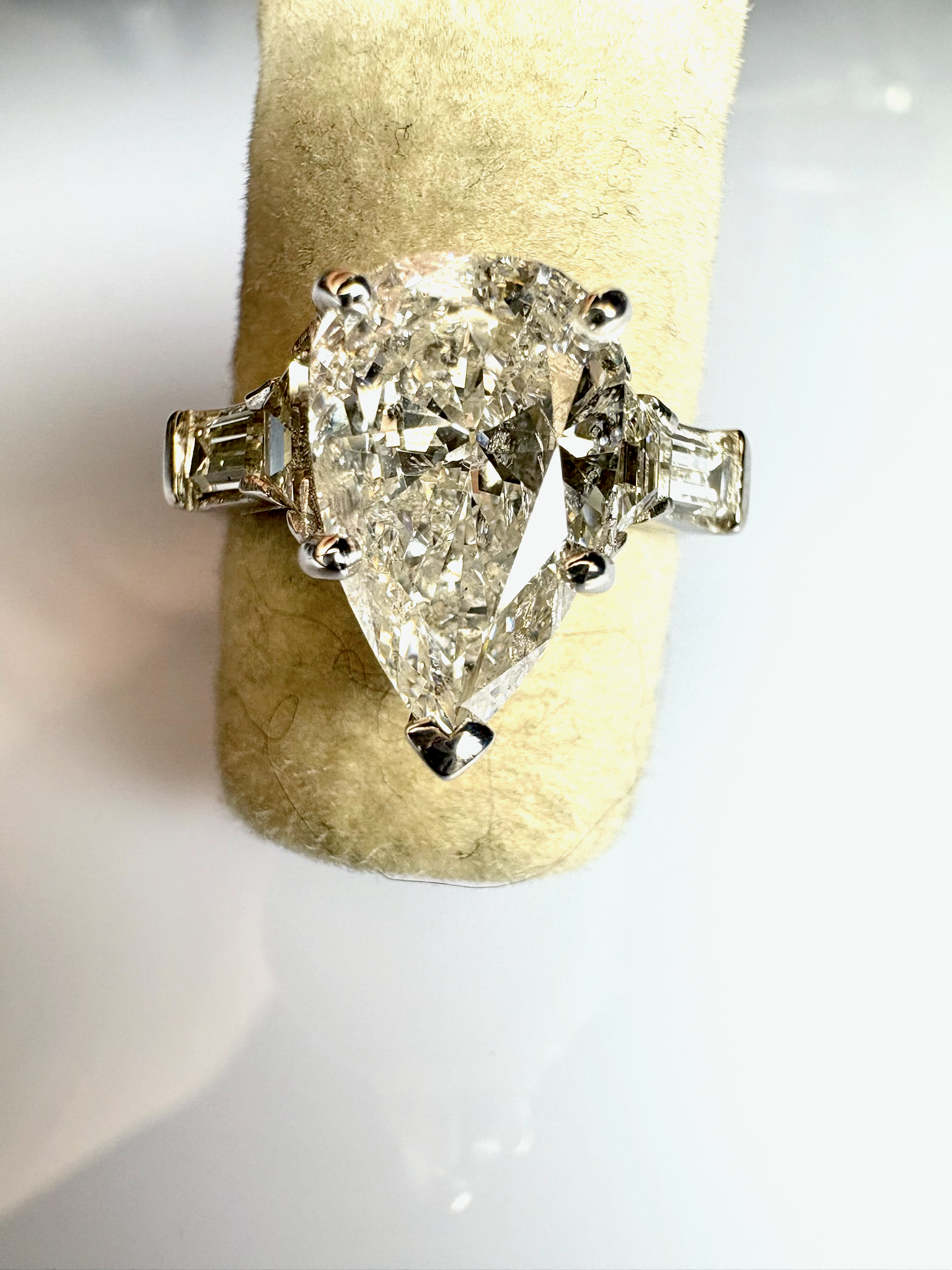 White gold teardrop-shaped diamond engagement ring with two smaller baguette-cut diamonds on sides.