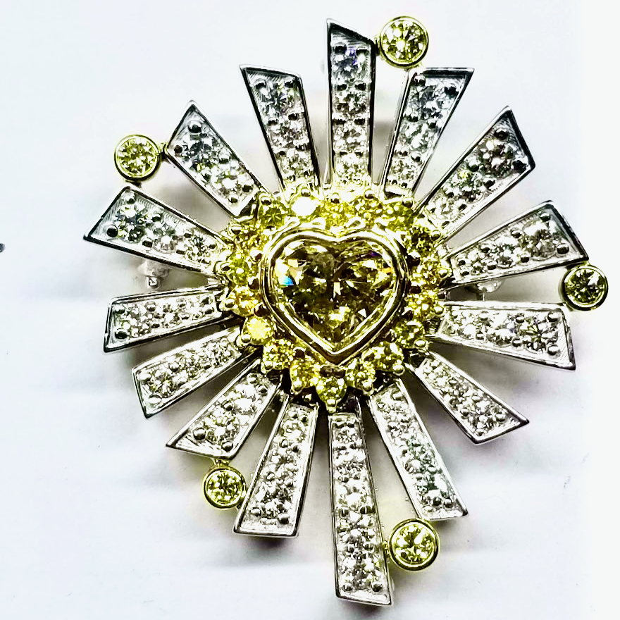 White and yellow gold mixed metal decorative brooch with a heart-shaped yellow diamond at the center, surrounded by yellow and clear diamonds, arranged in a radiating starburst pattern.