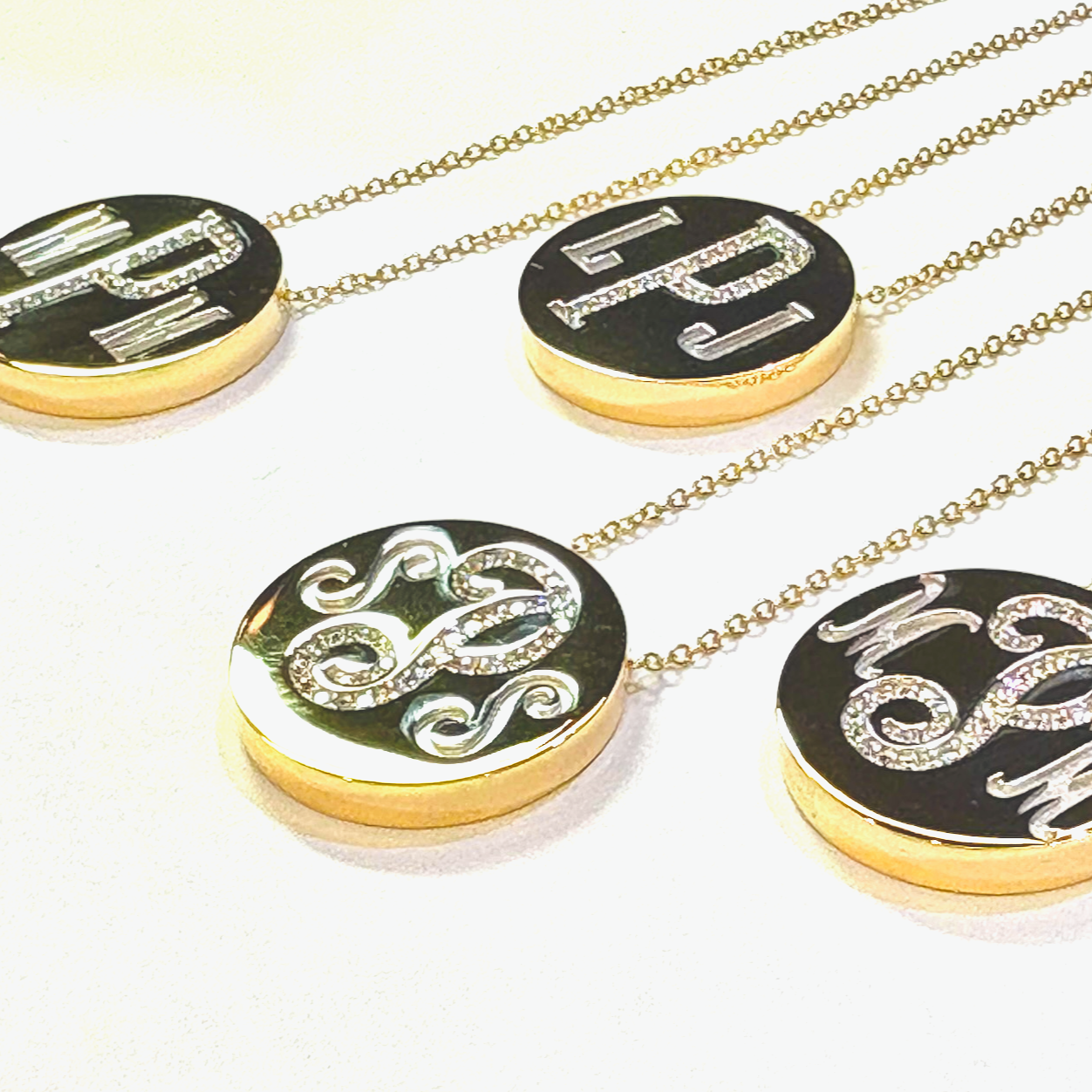 Four yellow gold monogram pendants on yellow gold chains.