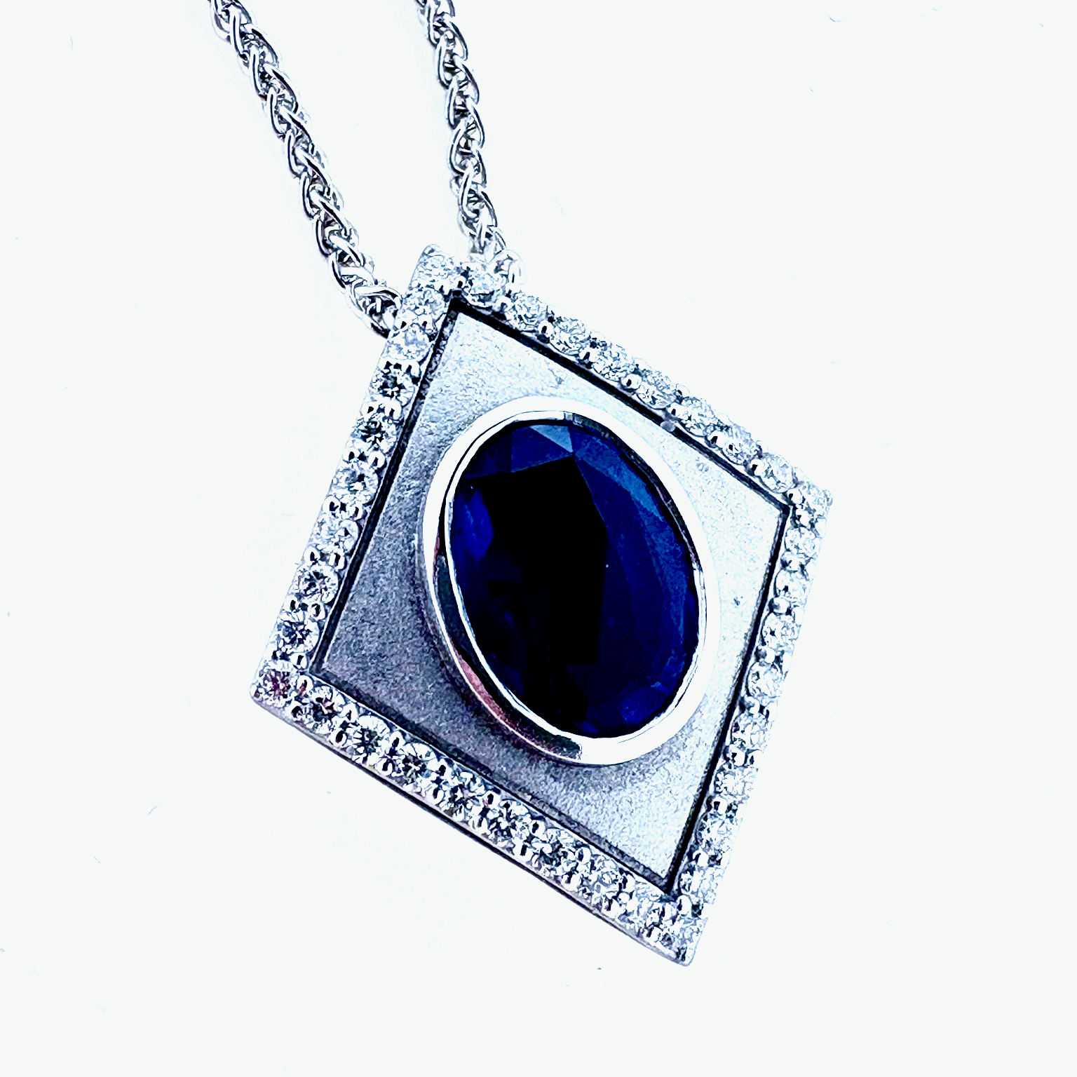 White gold pendant with large oval natural Sapphire and outlined with round radiant cut diamonds on a white gold chain.