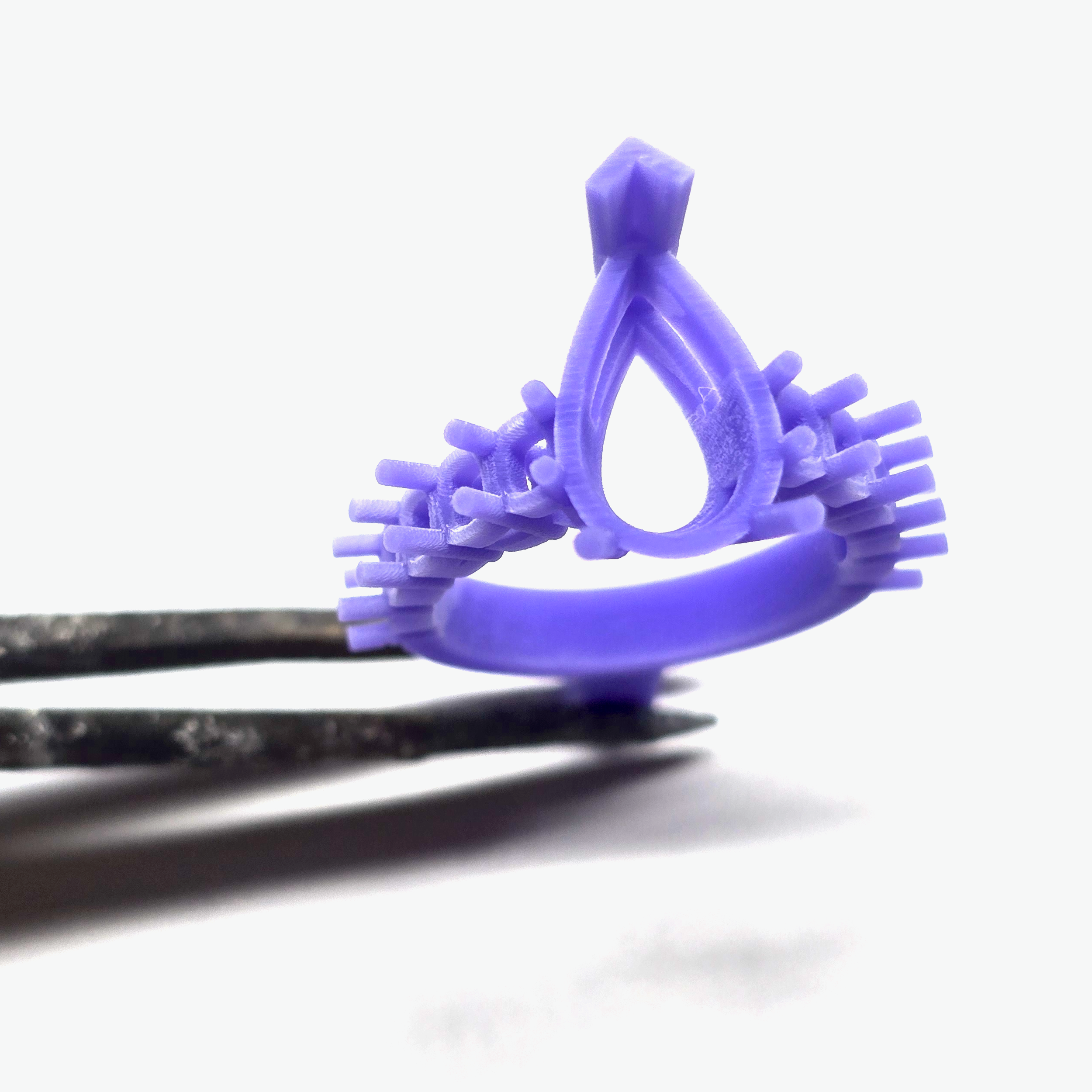 A close-up of a small, purple, 3D-printed wax mold for custom casting jewelry designs.