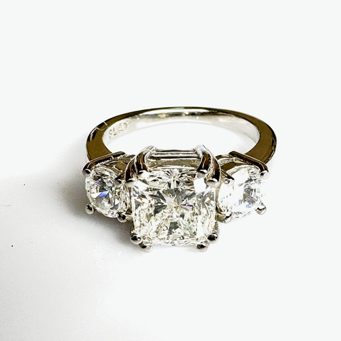 White gold engagment ring with one square cushion cut center diamond and 2 round radiant cut diamonds, prong set.