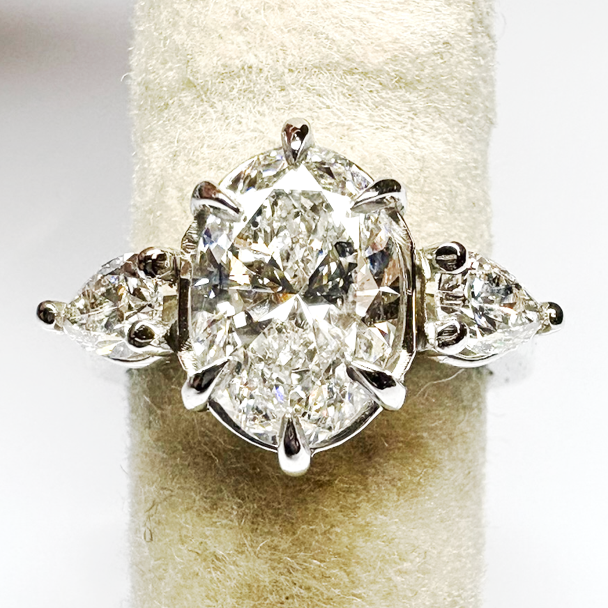 Diamond engagement ring with a central oval-cut diamond, flanked by two teardrop-cut diamonds, set in a white gold band.
