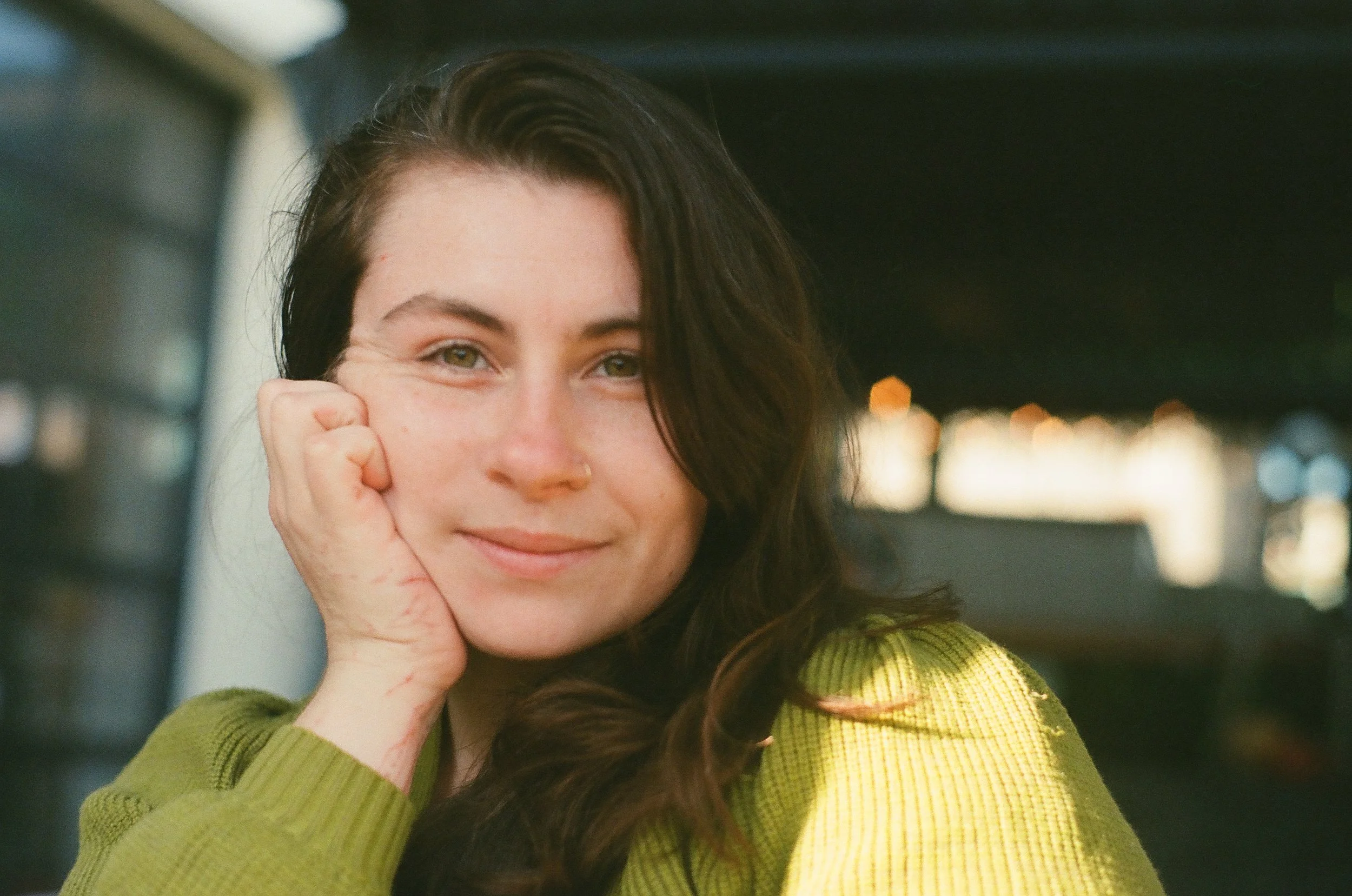 woman in green sweater, hand on cheek, smiling at camera