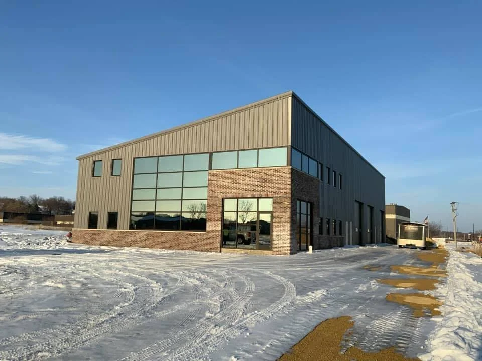 Modern two-story commercial building with brick and metal exterior, large glass windows, and snow-covered parking area.