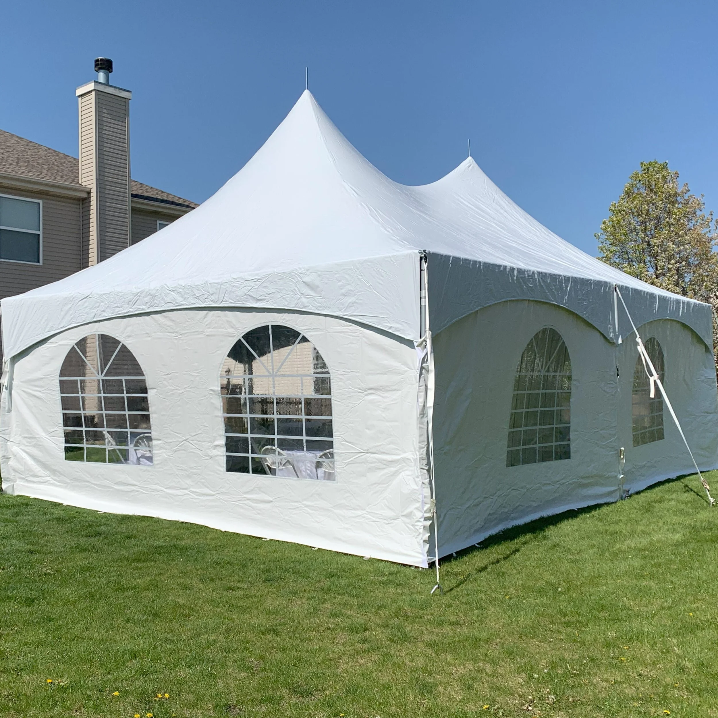 A white event tent with arched windows set up on a grassy yard against a blue sky.