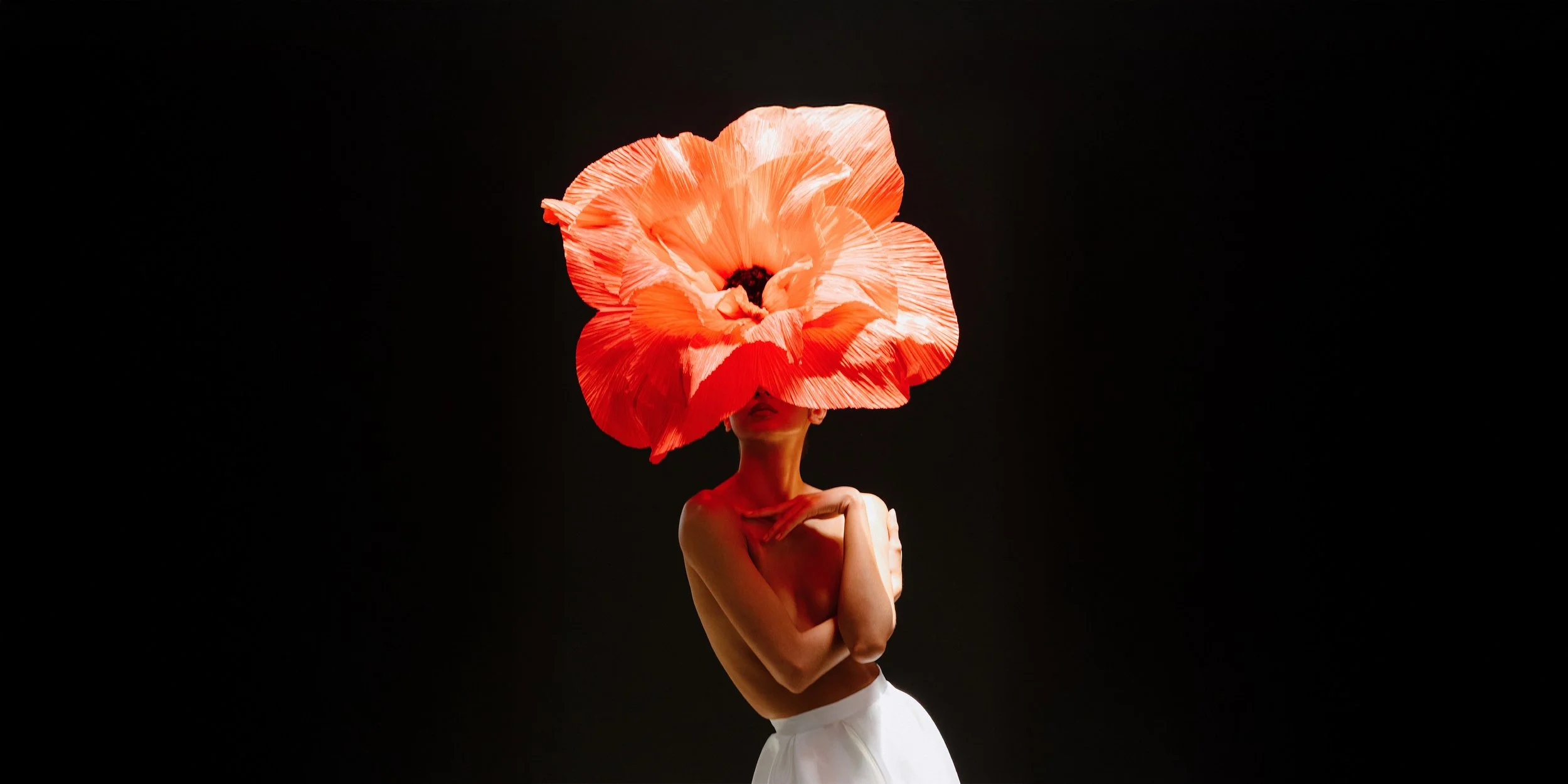 Persona con cuerpo desnudo usando un vestido blanco y cubriendo su rostro con una gran flor de color rosa