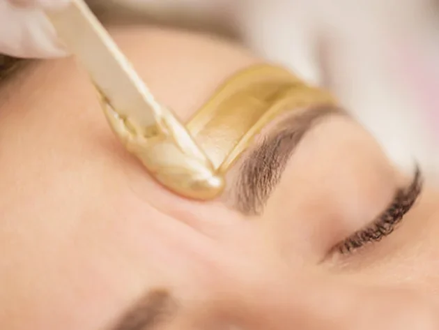 A person getting eyebrow waxing with wax being applied to the eyebrow.