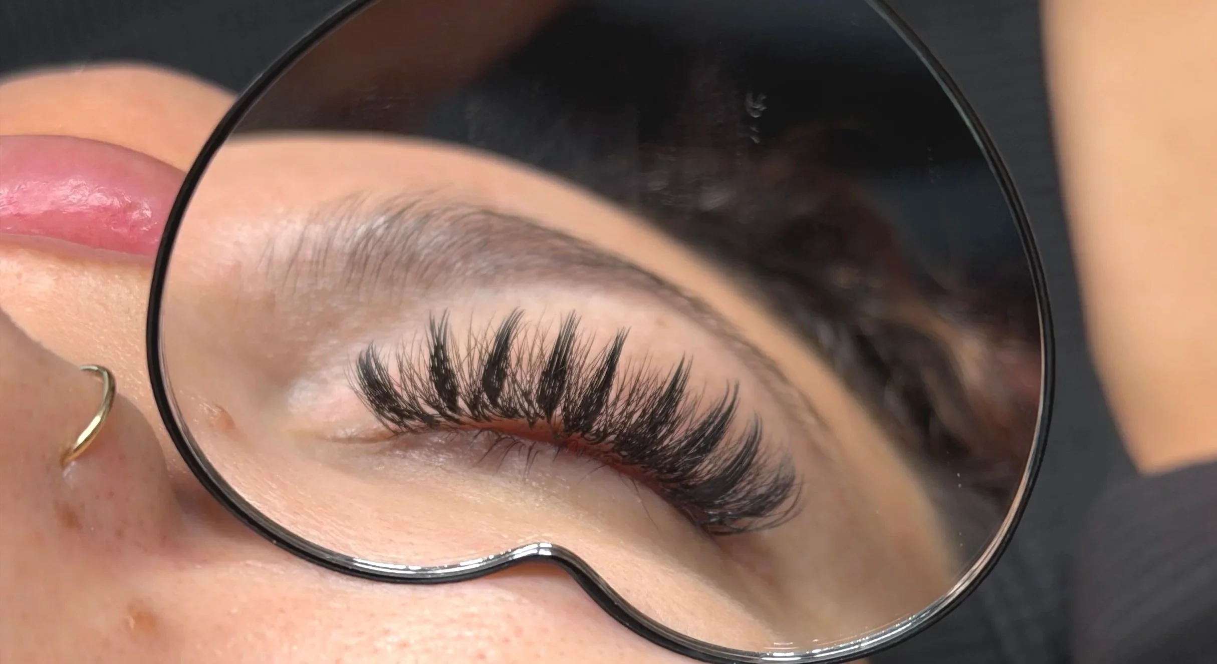 Close-up of a person's eye with long eyelashes seen through a magnifying mirror.
