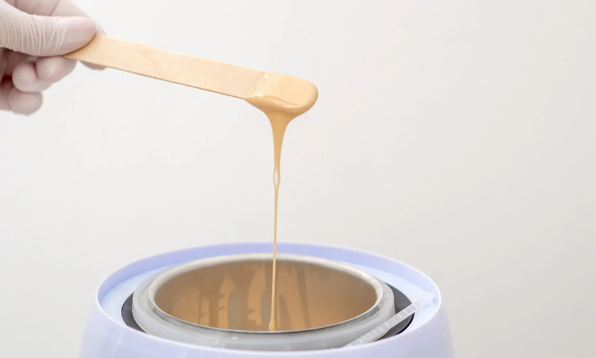 A gloved hand holding a wooden spatula with caramel ice cream above a cold stone ice cream maker.
