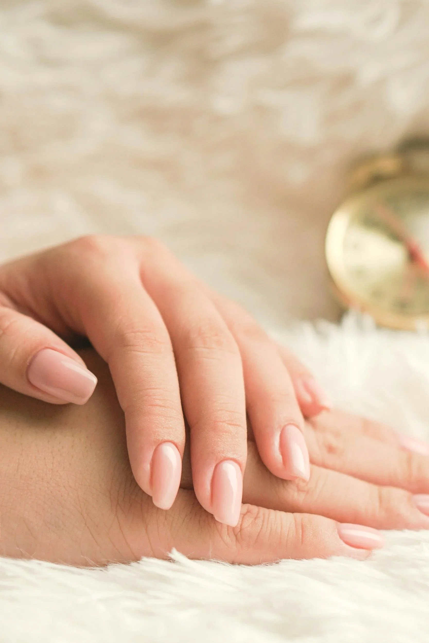 Close-up of a woman's hand resting on a soft, white surface, with a blurred clock in the background.