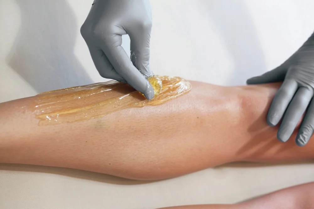 A person wearing gray gloves applying waxing to a person's leg for hair removal.