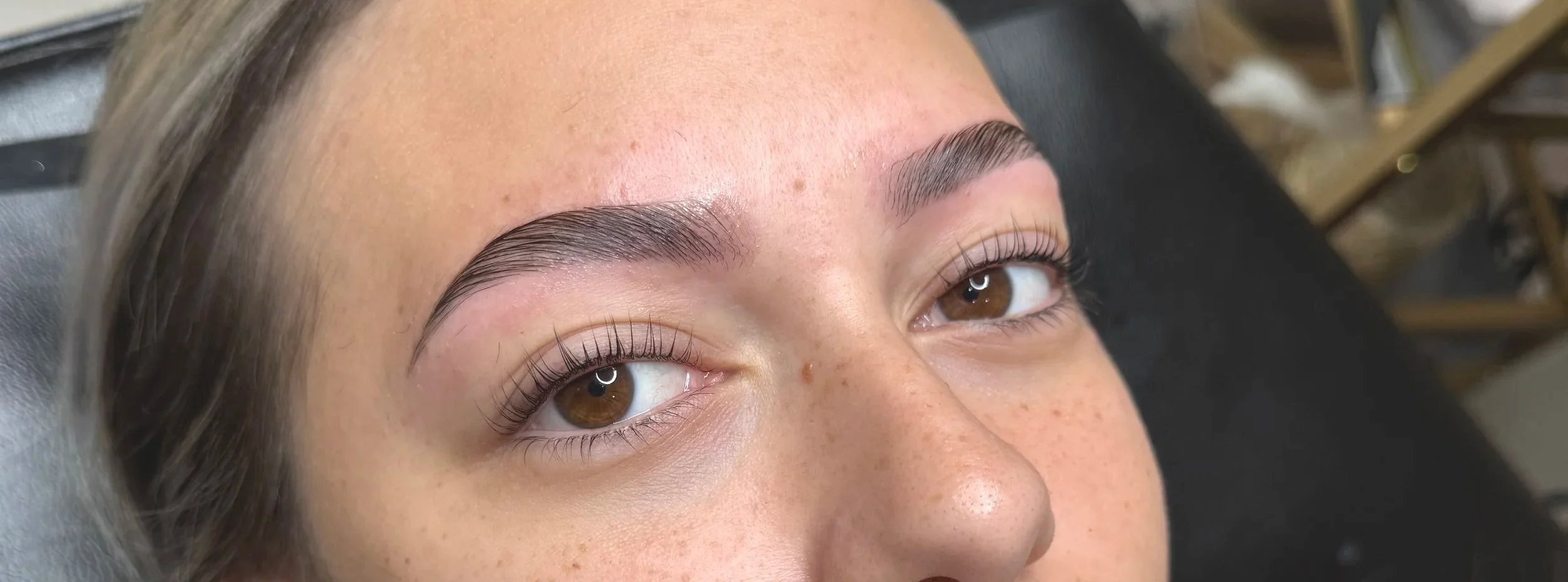 Close-up of a woman's face showing freshly done eyebrow microblading or permanent makeup.