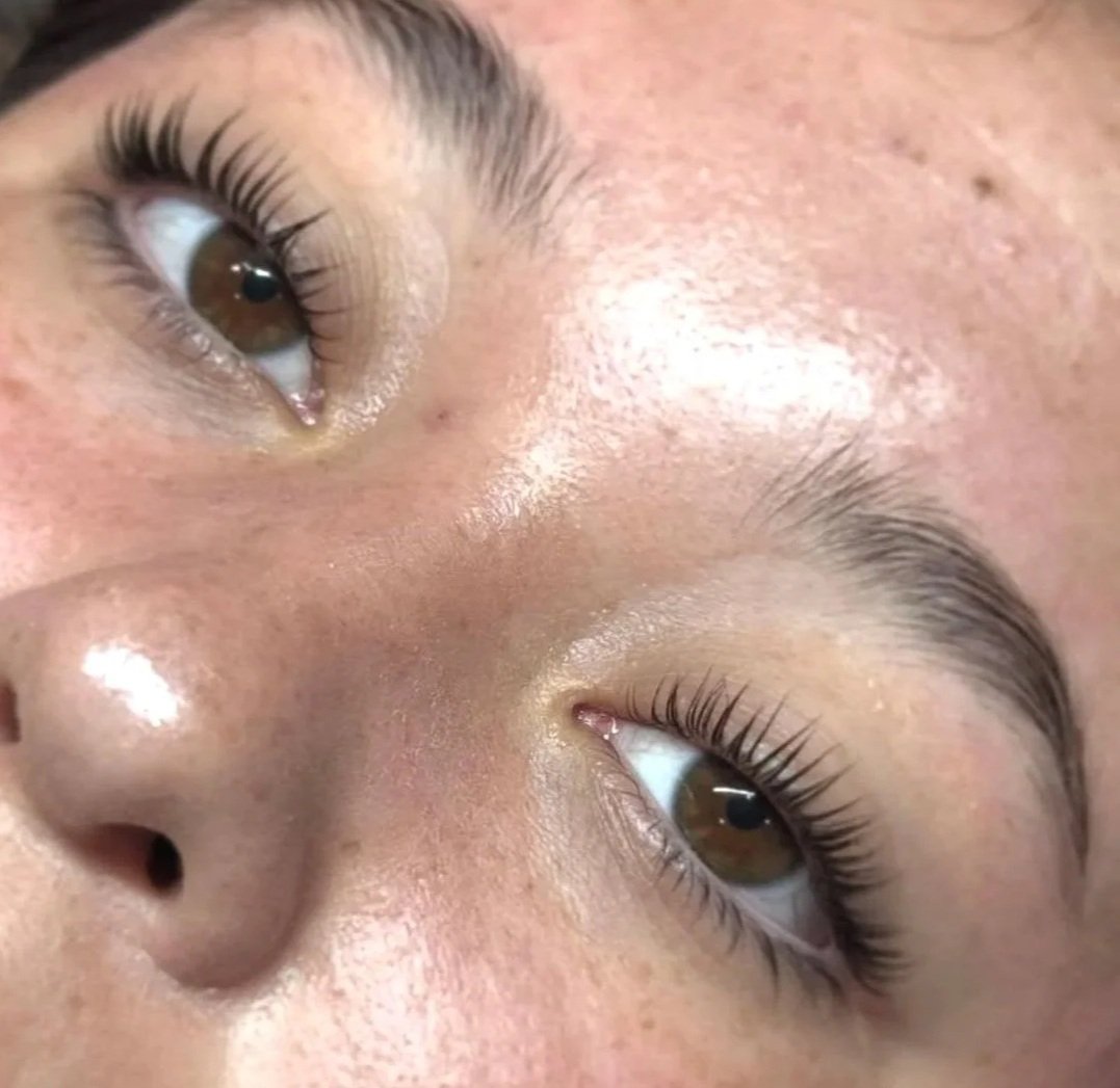 Close-up of a person's face focusing on brown eyes with naturally long eyelashes, smooth skin with visible pores, and eyebrows.