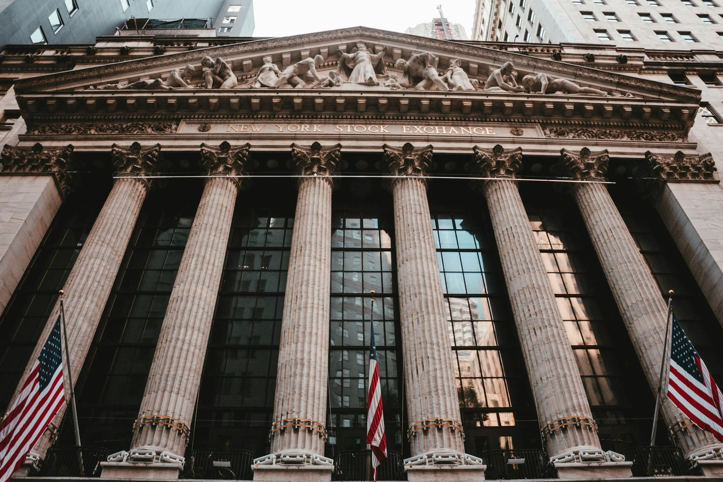 Front view of the New York Stock Exchange building with tall pillars, American flags, and classical architectural design.