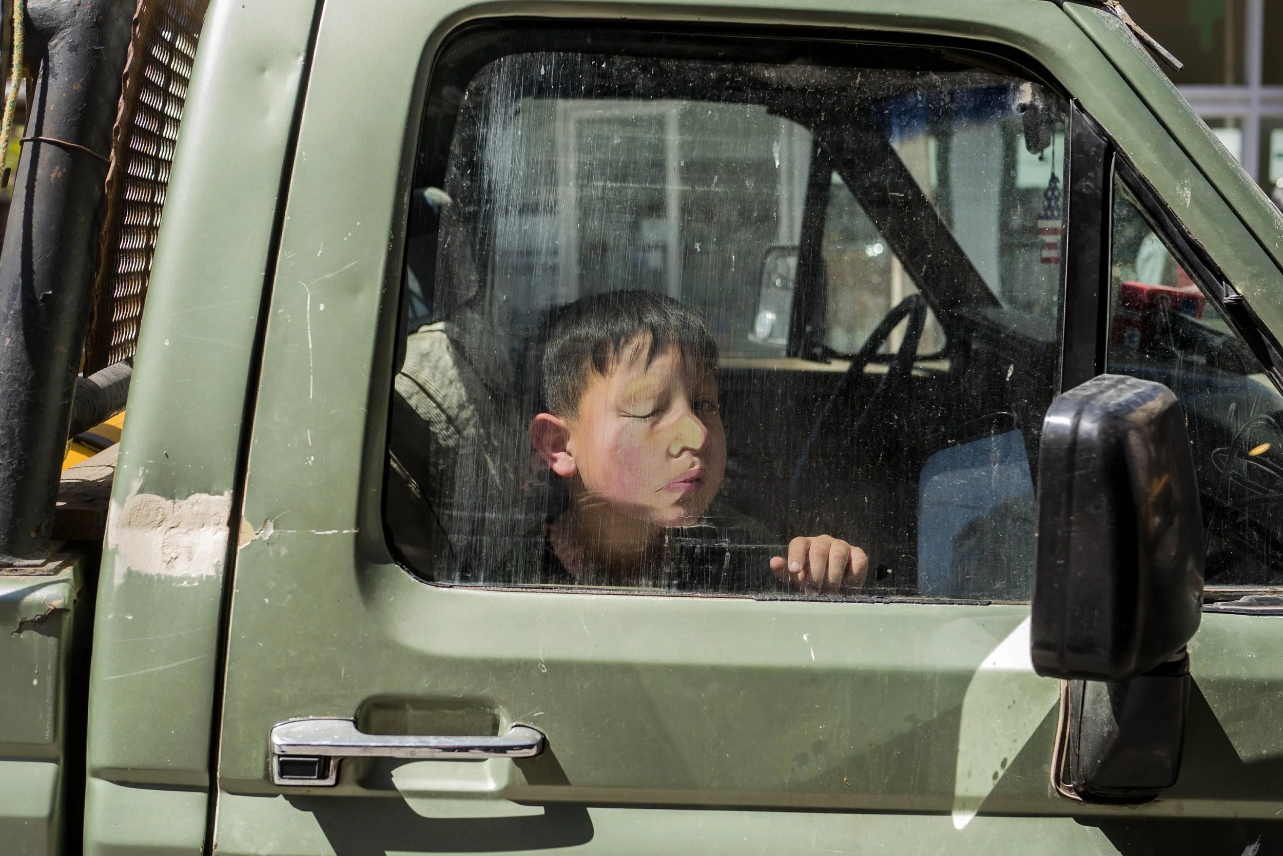 Niño dormido dentro de una camioneta vieja y sucia con cristales empañados.