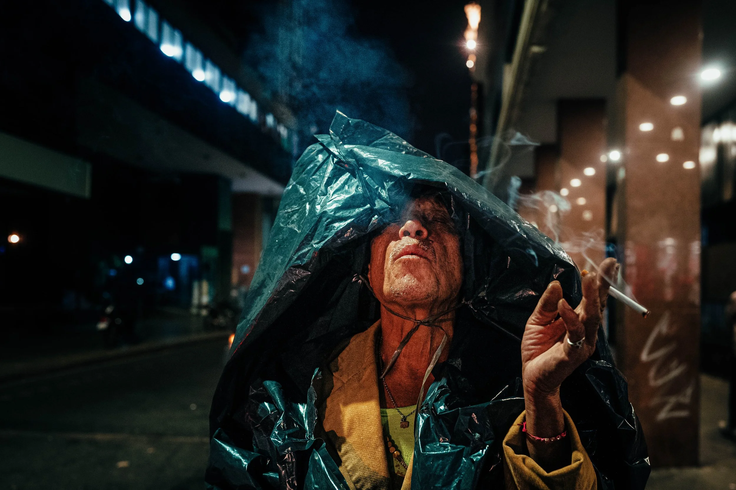 Persona mayor con sombrero de plástico fumando un cigarrillo en la calle de noche.