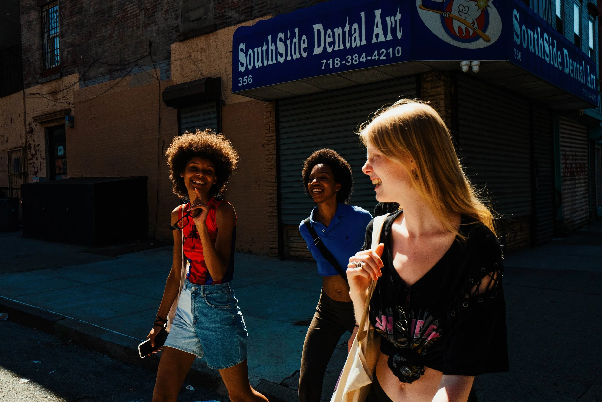 Tres jóvenes caminando y riendo en la calle frente a un negocio llamado SouthSide Dental Art.