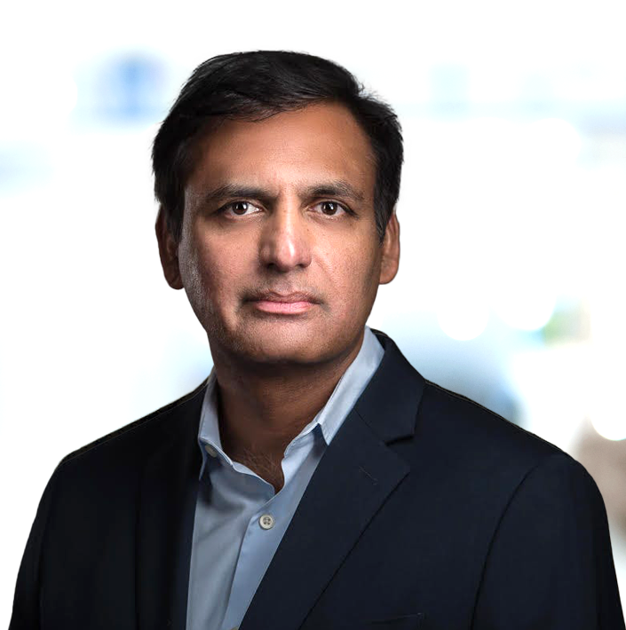 Professional portrait of Praveen Tipirneni, MD, MBA Chief Executive Officer of Caldera Therapeutics in a dark suit and light blue shirt against a blurred background.