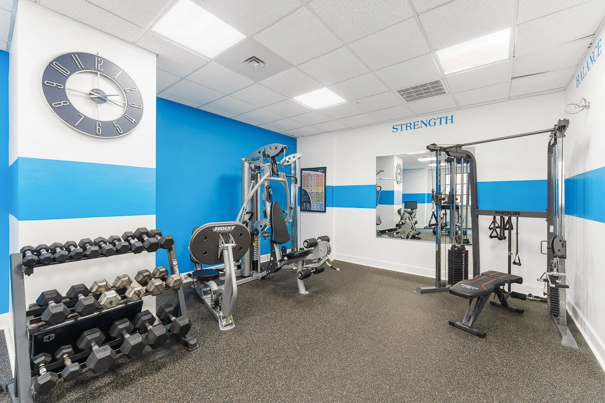 Real Estate photo of a condo gym with various workout equipment including dumbbells, weight machines, and a bench.
