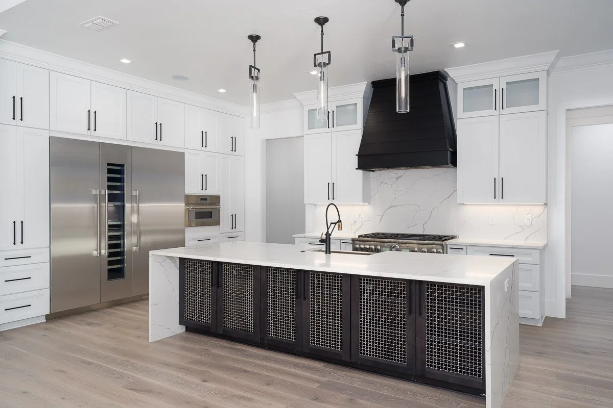 Modern kitchen with white cabinetry, marble backsplash and countertop, black range hood, stainless steel refrigerator, oven, and a kitchen island with a black base and white marble top.