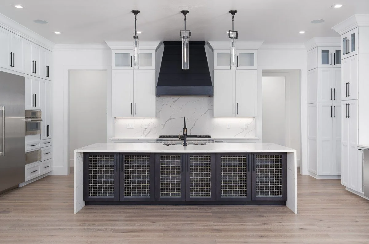 Modern kitchen with white cabinets, black hardware, a large island with a black base and white marble countertop, stainless steel appliances, and three pendant lights hanging above the island.
