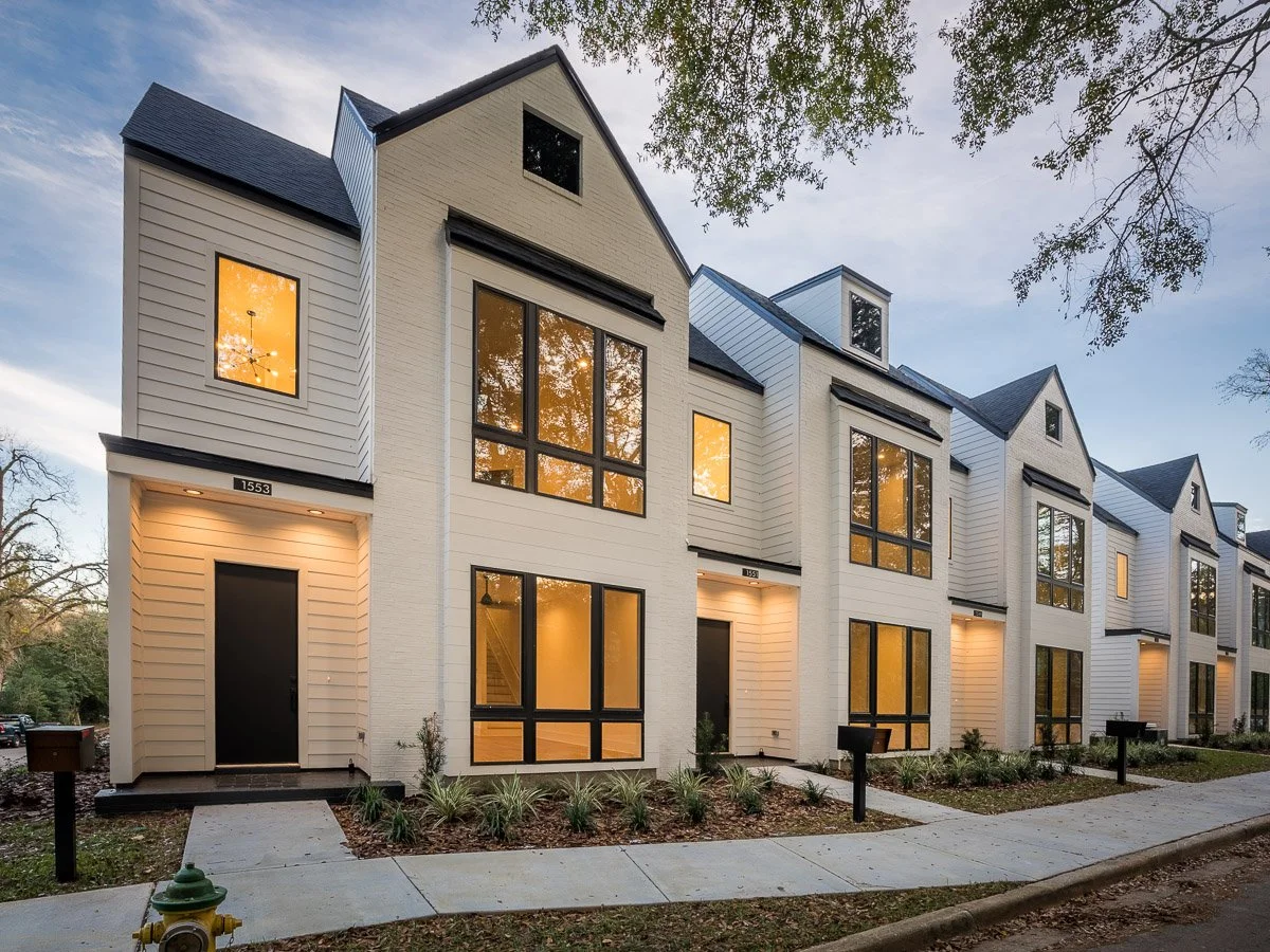 Real Estate photo of a modern multi-story townhouse with large front windows and well-lit entrances at dusk.